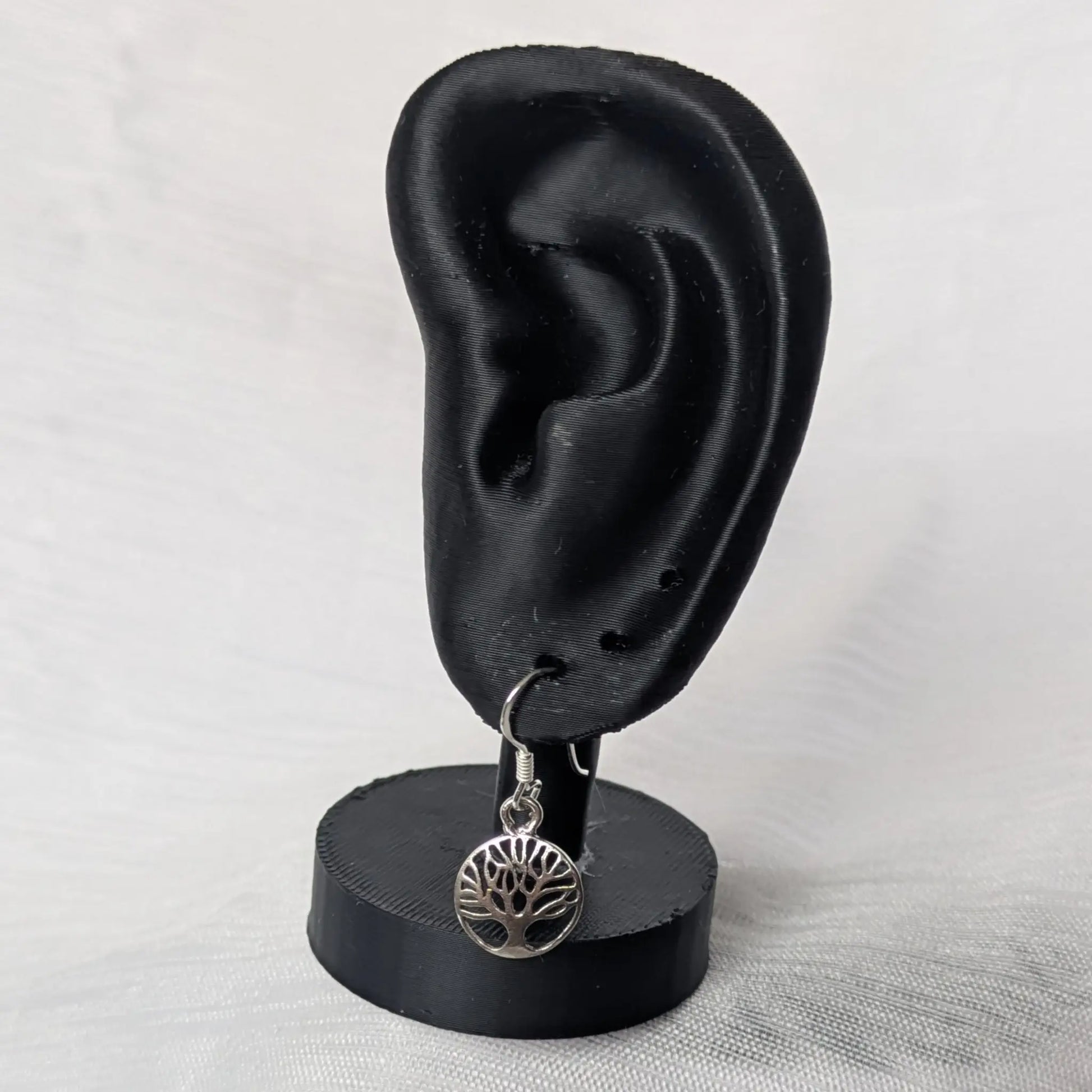 Elegante Lebensbaum-Silberohrringe hängend an einem schwarzen Schmuck-Display.