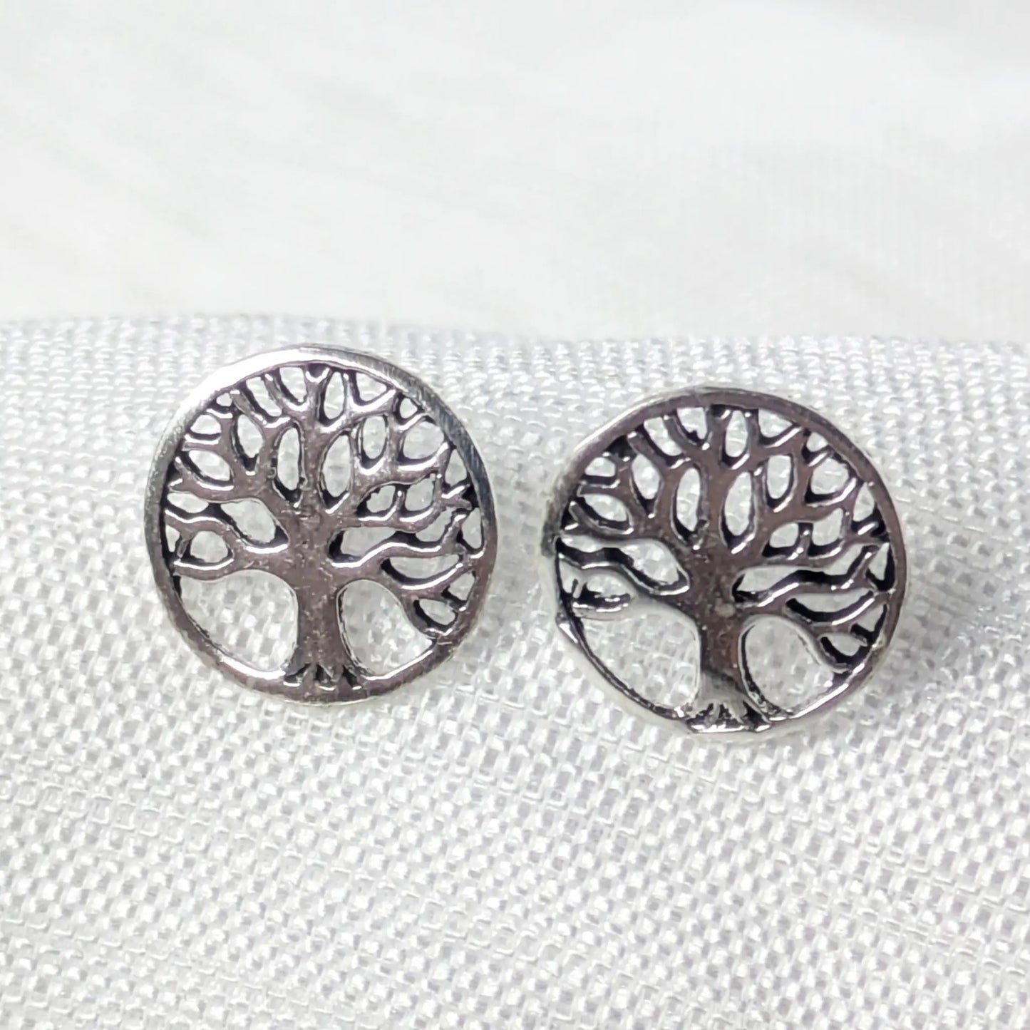 Nahaufnahme von einem Paar runder 925 Silber-Ohrstecker mit filigranem Lebensbaum-Motiv auf weißem Strukturstoff.