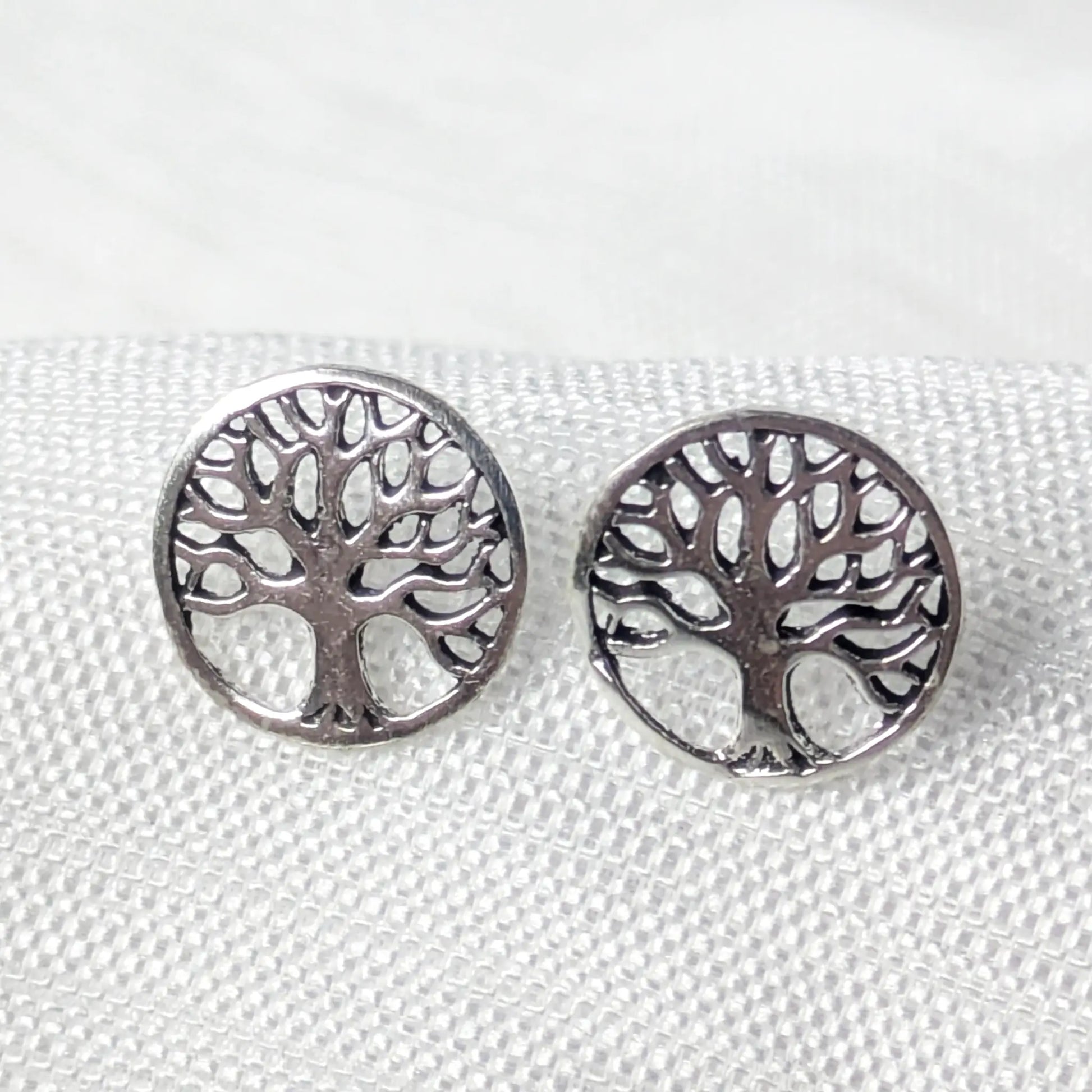 Nahaufnahme von einem Paar runder 925 Silber-Ohrstecker mit filigranem Lebensbaum-Motiv auf weißem Strukturstoff.