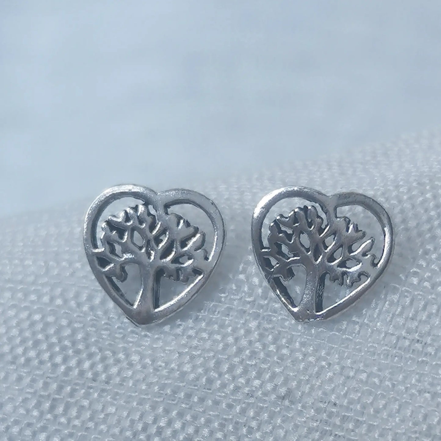 Nahaufnahme von zwei herzförmigen Ohrsteckern aus 925 Silber mit filigran eingearbeitetem Lebensbaum-Motiv.