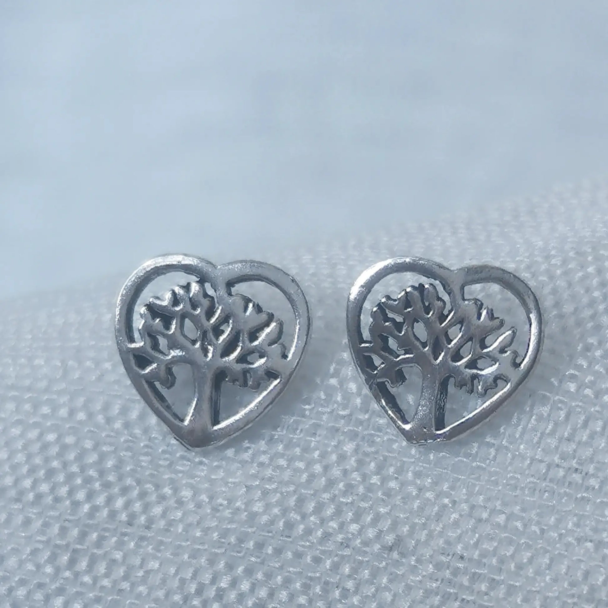 Nahaufnahme von zwei herzförmigen Ohrsteckern aus 925 Silber mit filigran eingearbeitetem Lebensbaum-Motiv.