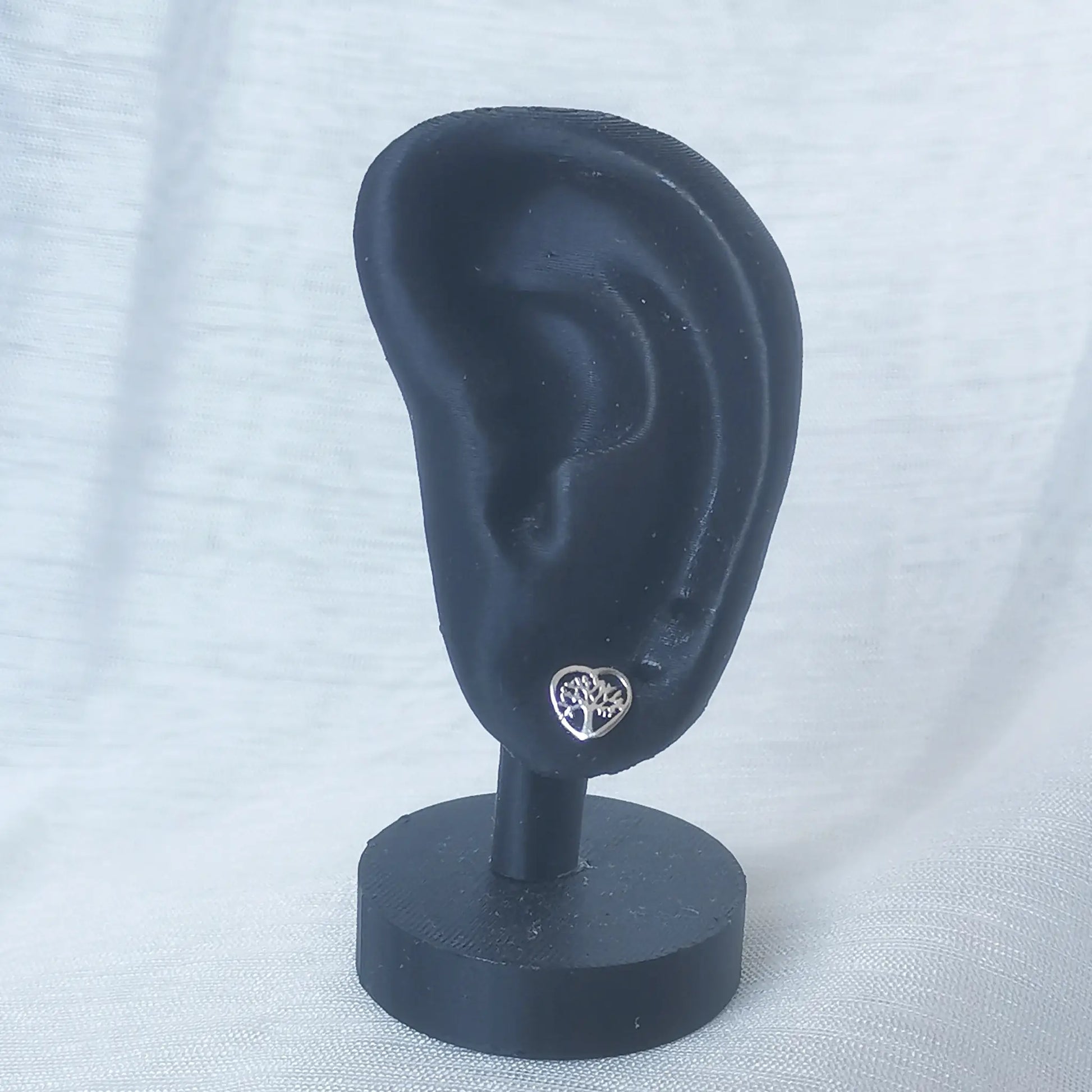 Ein silberner Herz-Ohrstecker mit Lebensbaum, getragen an einem schwarzen Ohr-Display zur optimalen Veranschaulichung der Größe.