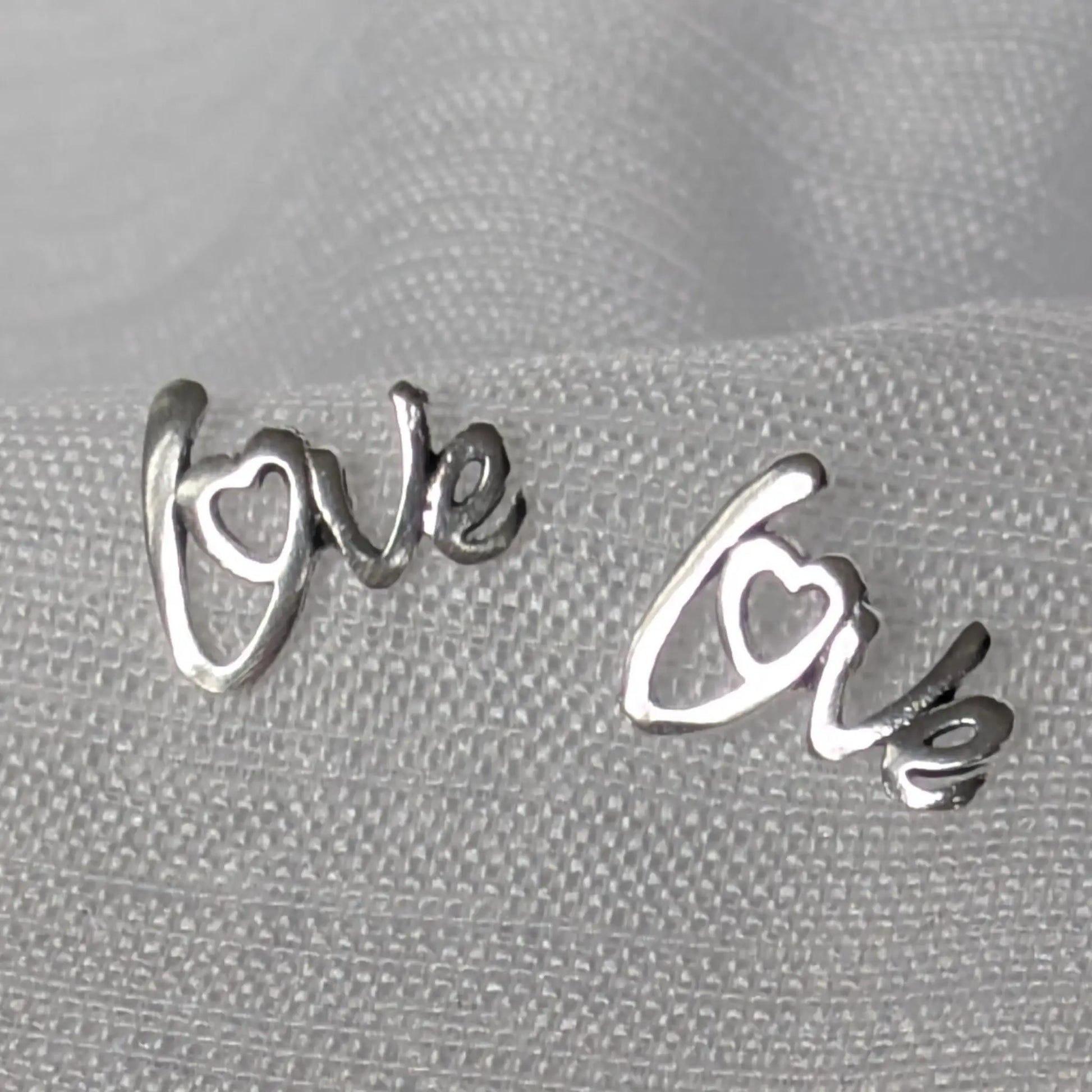 Paar silberne Love-Ohrstecker aus 925 Sterling Silber in der Vorderansicht auf hellem Stoff.