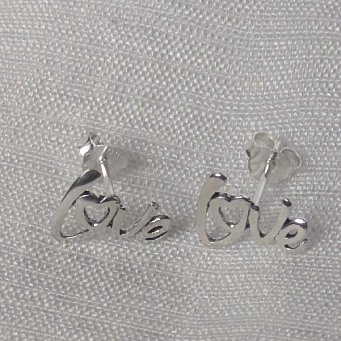 Minimalistische Love-Schriftzug-Ohrringe aus echtem Silber auf weißem, neutralem Hintergrund.