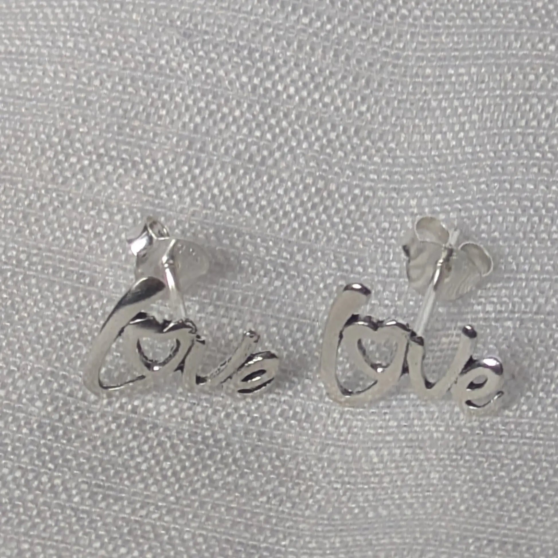 Minimalistische Love-Schriftzug-Ohrringe aus echtem Silber auf weißem, neutralem Hintergrund.