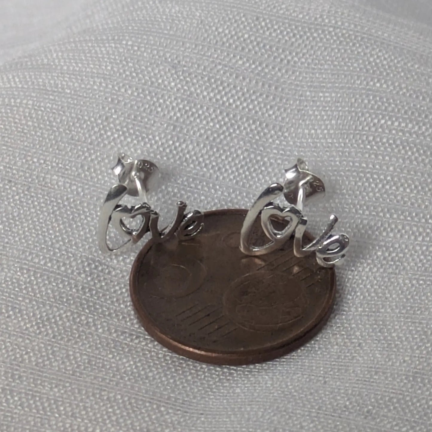 Größenvergleich der silbernen Herz-Ohrstecker auf einer 5-Cent-Münze platziert.