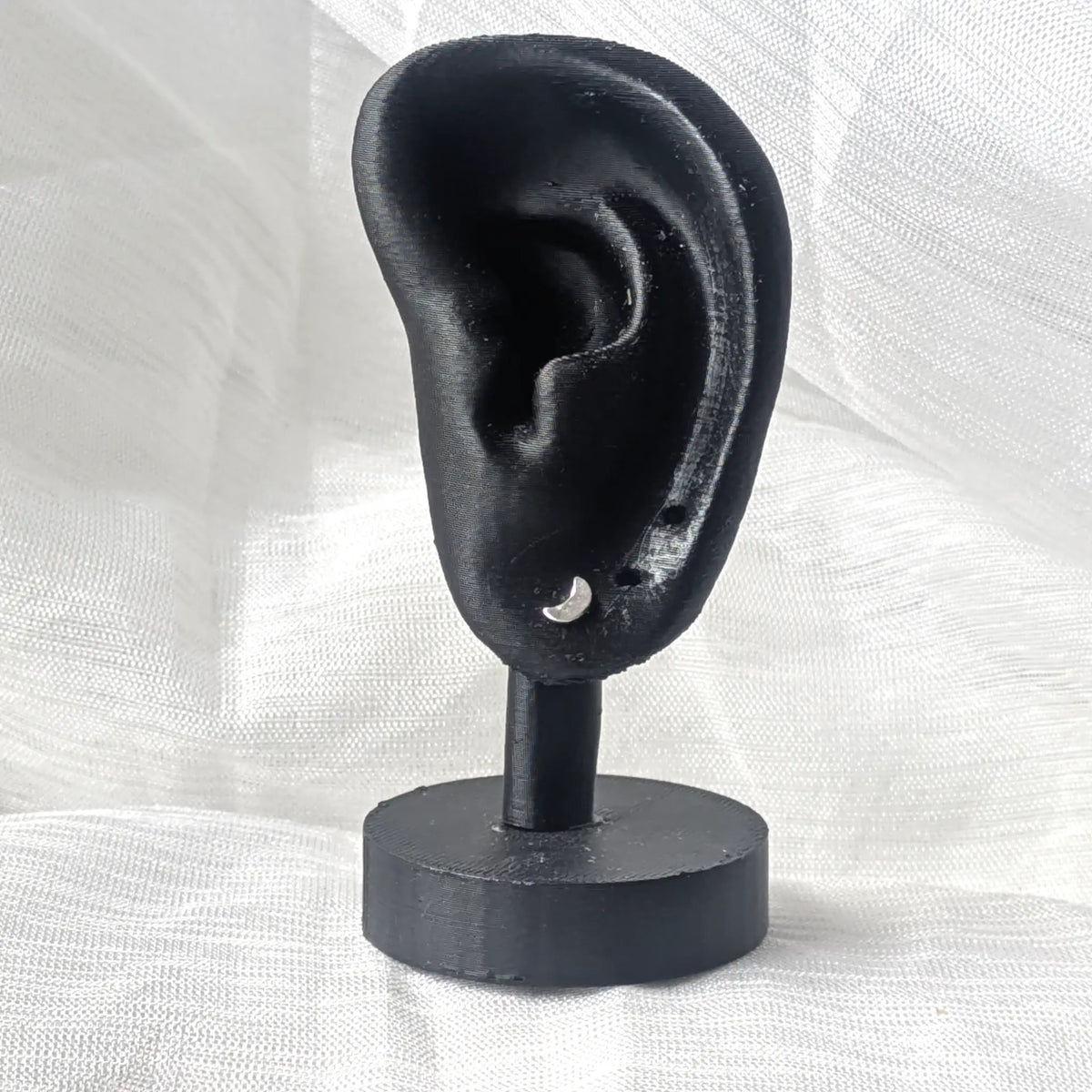 Ein einzelner zierlicher silberner Mond-Ohrstecker, minimalistisch an einem schwarzen Ohr-Display präsentiert.