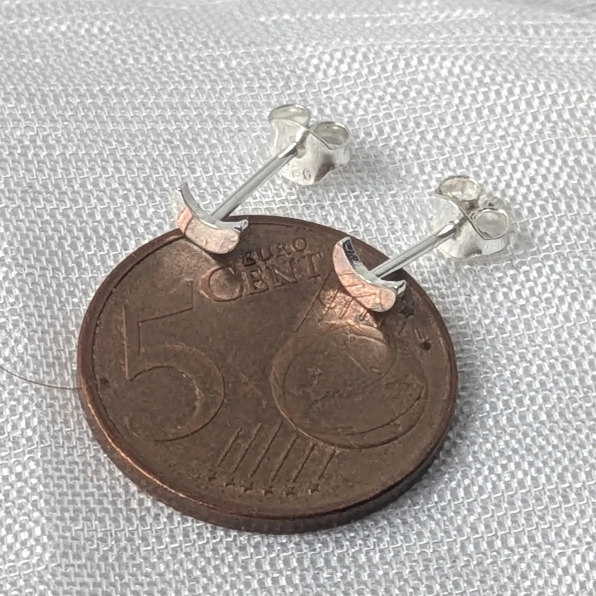 Kleine Halbmond-Silberohrstecker, direkt auf einer 5-Cent-Münze platziert, um die zierliche Größe zu veranschaulichen.