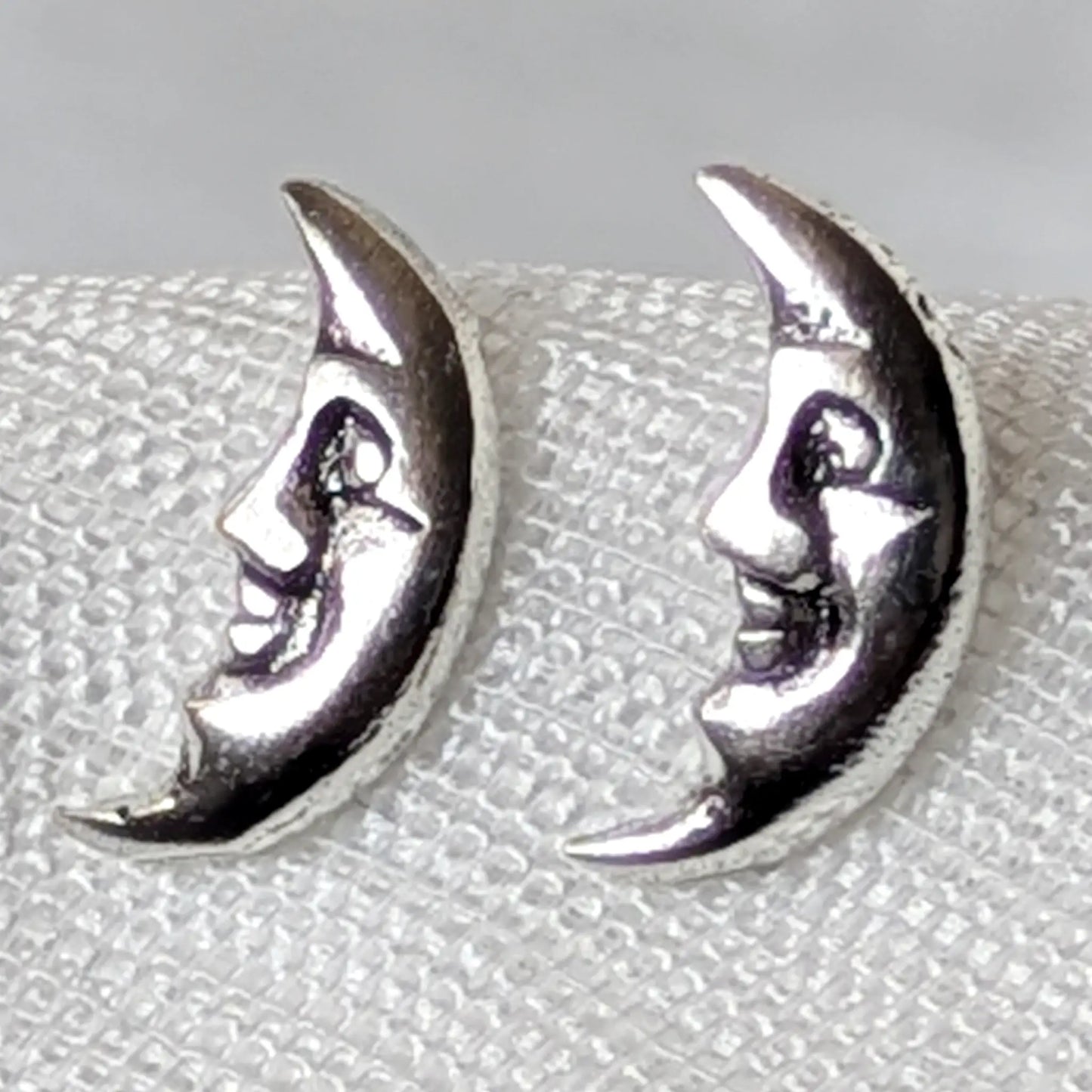 Nahaufnahme von zwei filigranen Mondgesicht-Ohrsteckern aus glänzendem 925 Silber mit detaillierten Gesichtern.