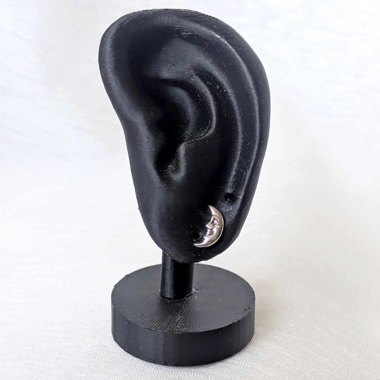 Ein kleiner silberner Ohrstecker mit Mondgesicht, elegant präsentiert an einem schwarzen Ohr-Display.