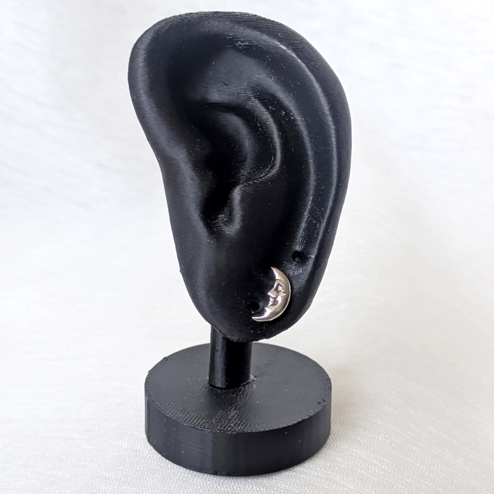 Ein kleiner silberner Ohrstecker mit Mondgesicht, elegant präsentiert an einem schwarzen Ohr-Display.