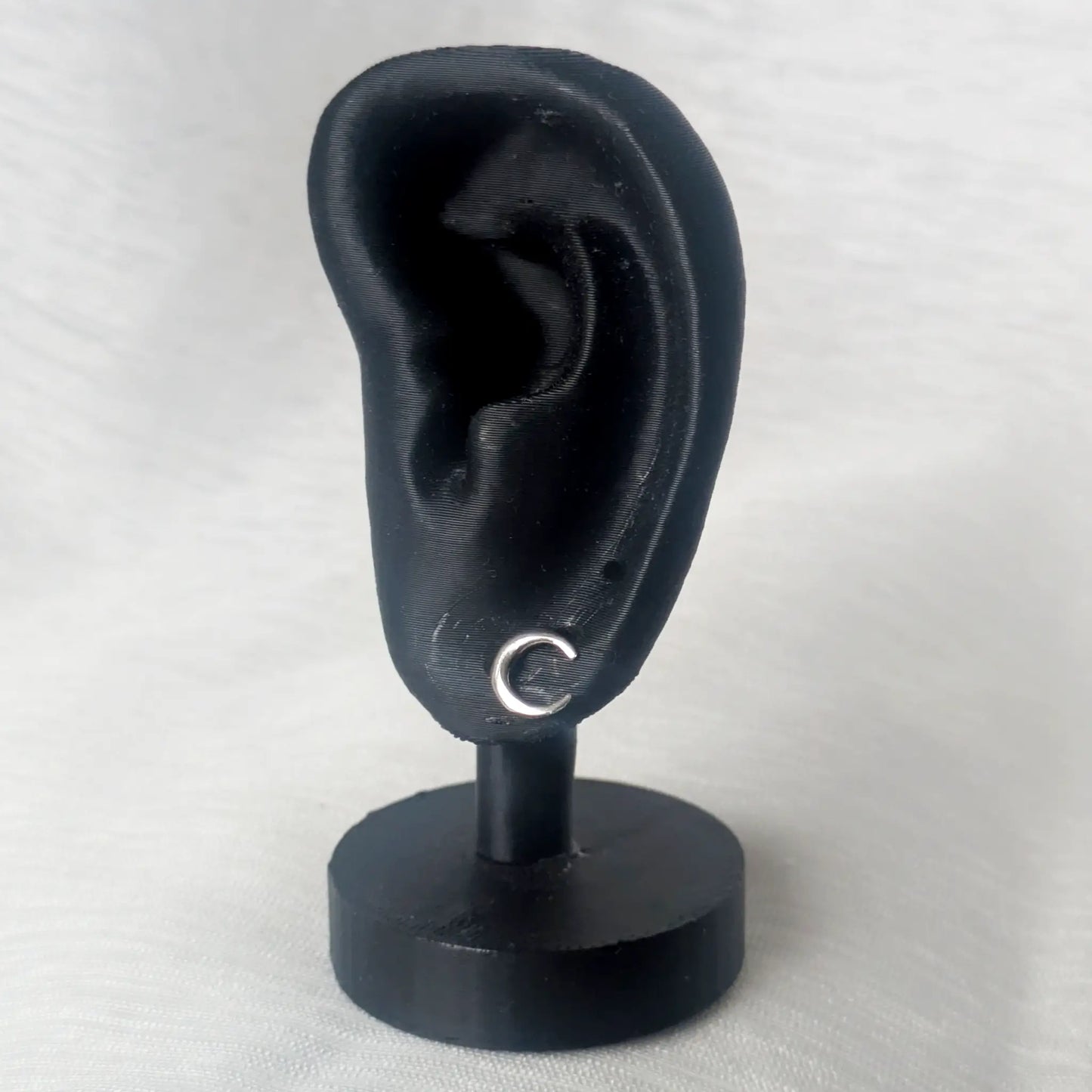 Ein einzelner silberner Halbmond-Ohrstecker präsentiert an einem schwarzen Ohr-Display veranschaulicht die filigrane Wirkung am Ohr.