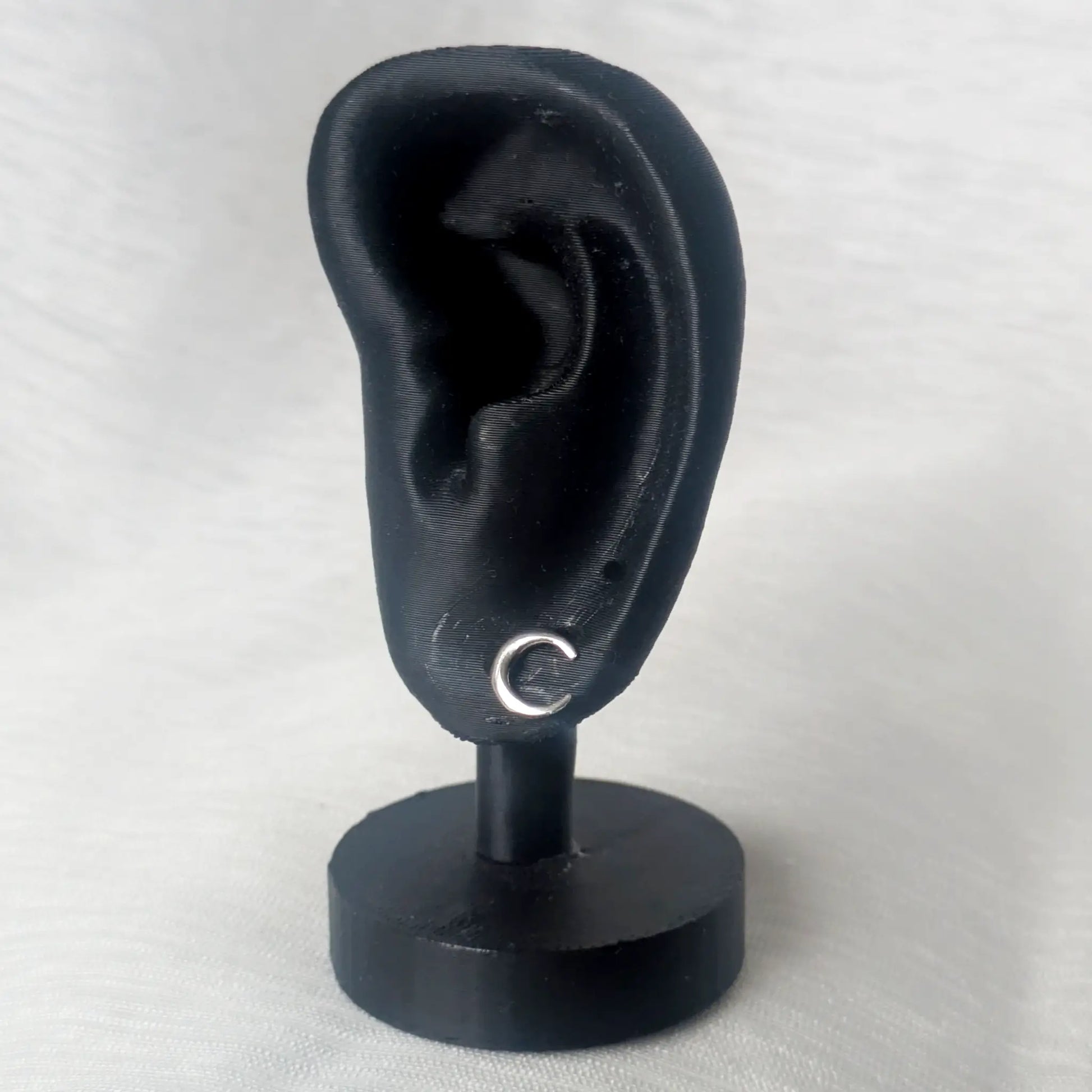 Ein einzelner silberner Halbmond-Ohrstecker präsentiert an einem schwarzen Ohr-Display veranschaulicht die filigrane Wirkung am Ohr.