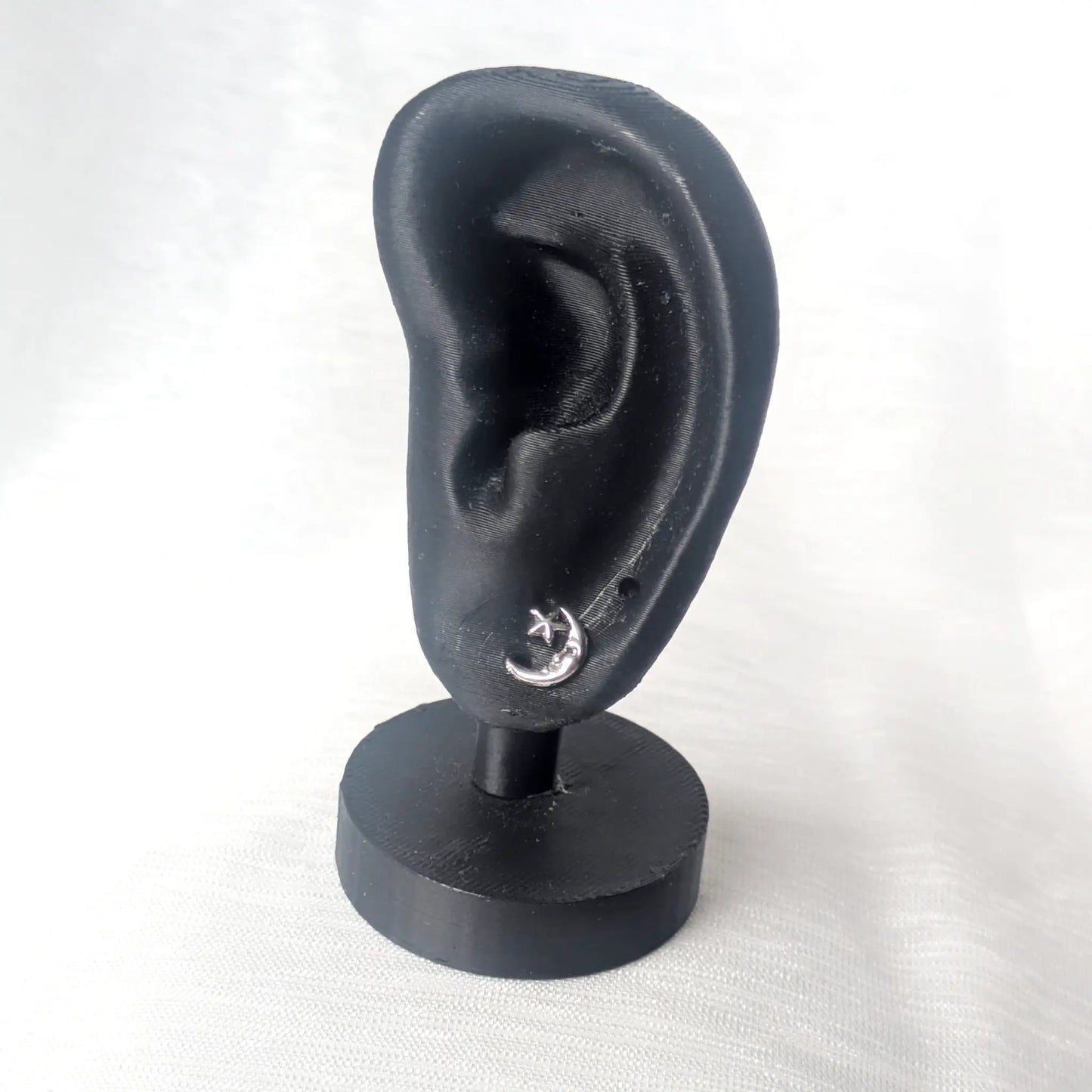 Ein filigraner Mond-Ohrstecker getragen an einem schwarzen Ohr-Modell zeigt die feinen Proportionen des Schmuckstücks.