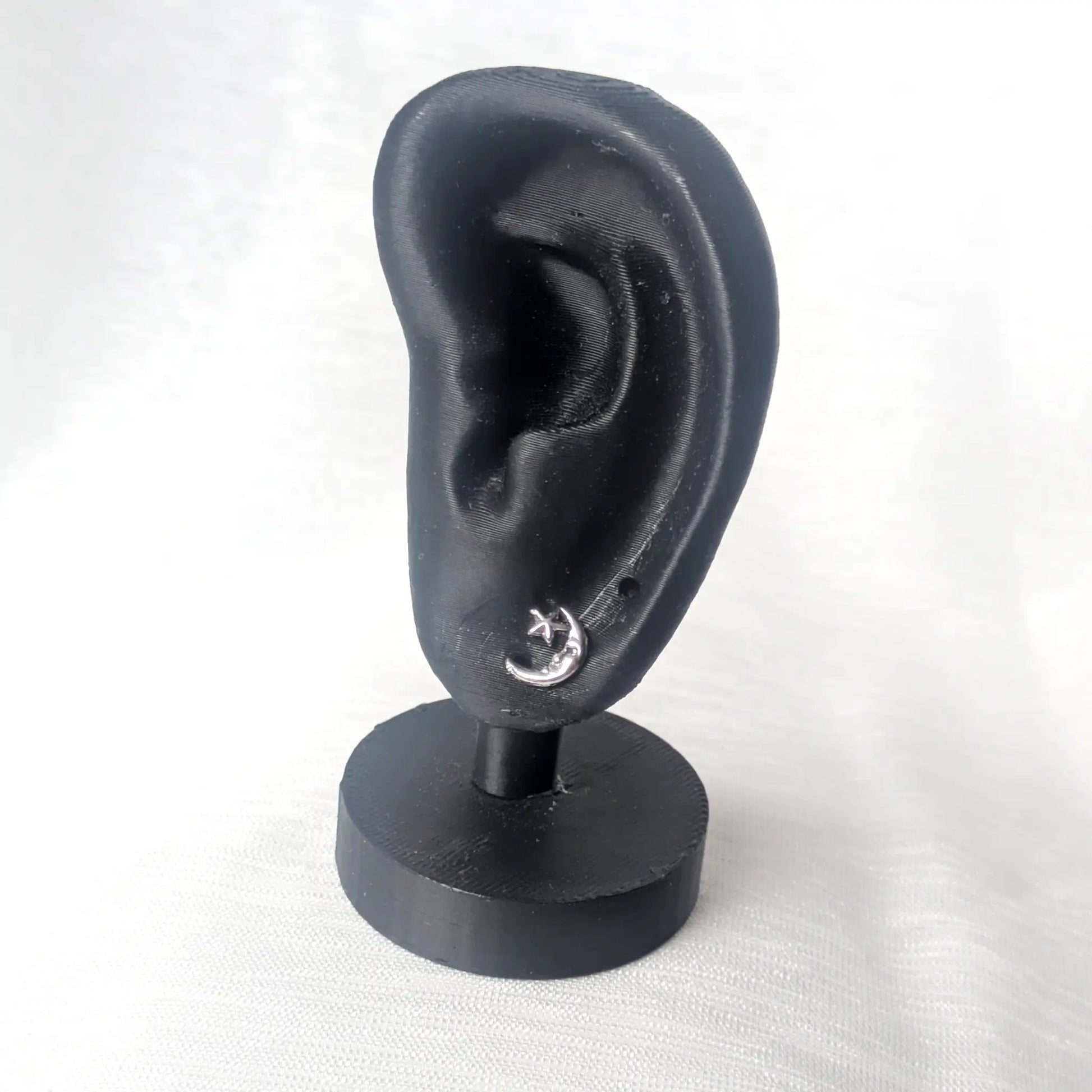 Ein filigraner Mond-Ohrstecker getragen an einem schwarzen Ohr-Modell zeigt die feinen Proportionen des Schmuckstücks.