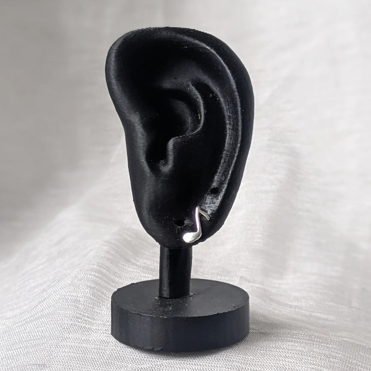 Ein einzelner silberner Achtelnoten-Ohrstecker, stilvoll präsentiert an einem schwarzen 3D-Ohr-Display.