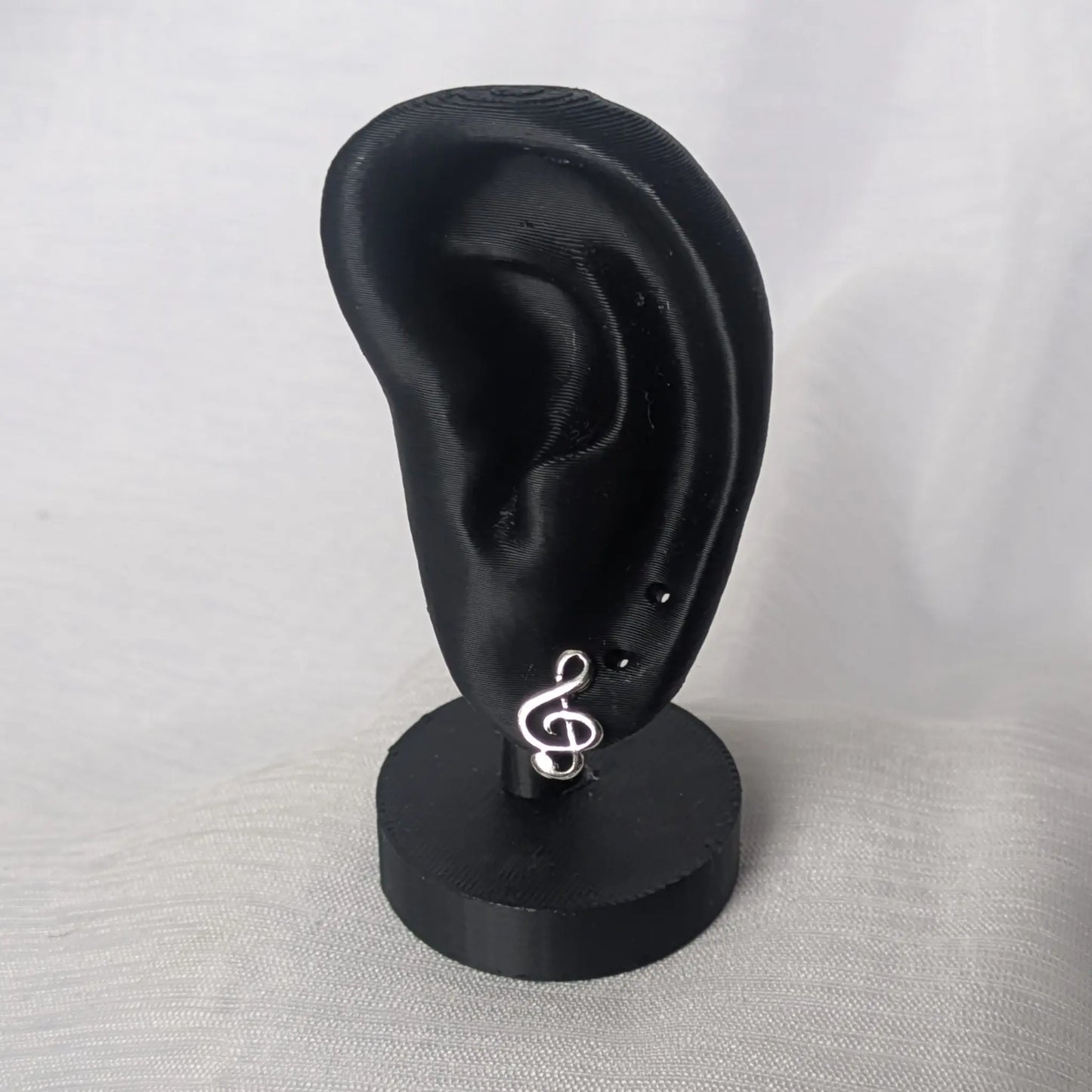 Elegante Notenschlüssel-Ohrstecker auf einem schwarzen Display zur Größendarstellung.