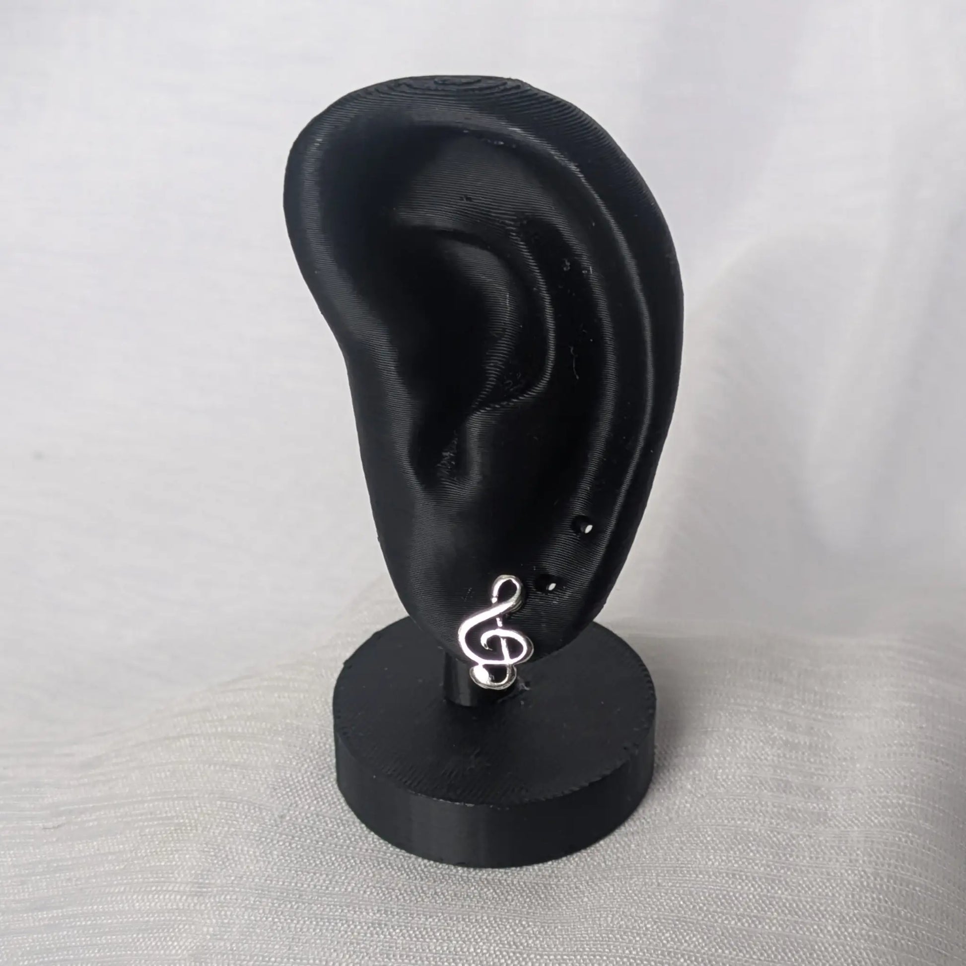 Elegante Notenschlüssel-Ohrstecker auf einem schwarzen Display zur Größendarstellung.