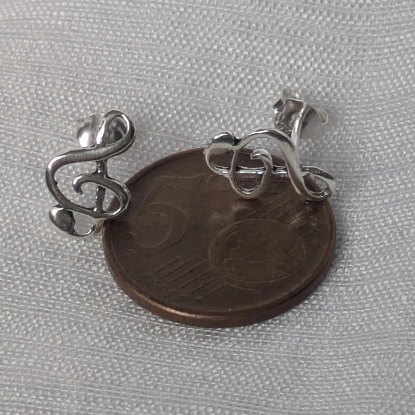 Größenvergleich der silbernen Violinschlüssel-Ohrstecker auf einer 5-Cent-Münze.