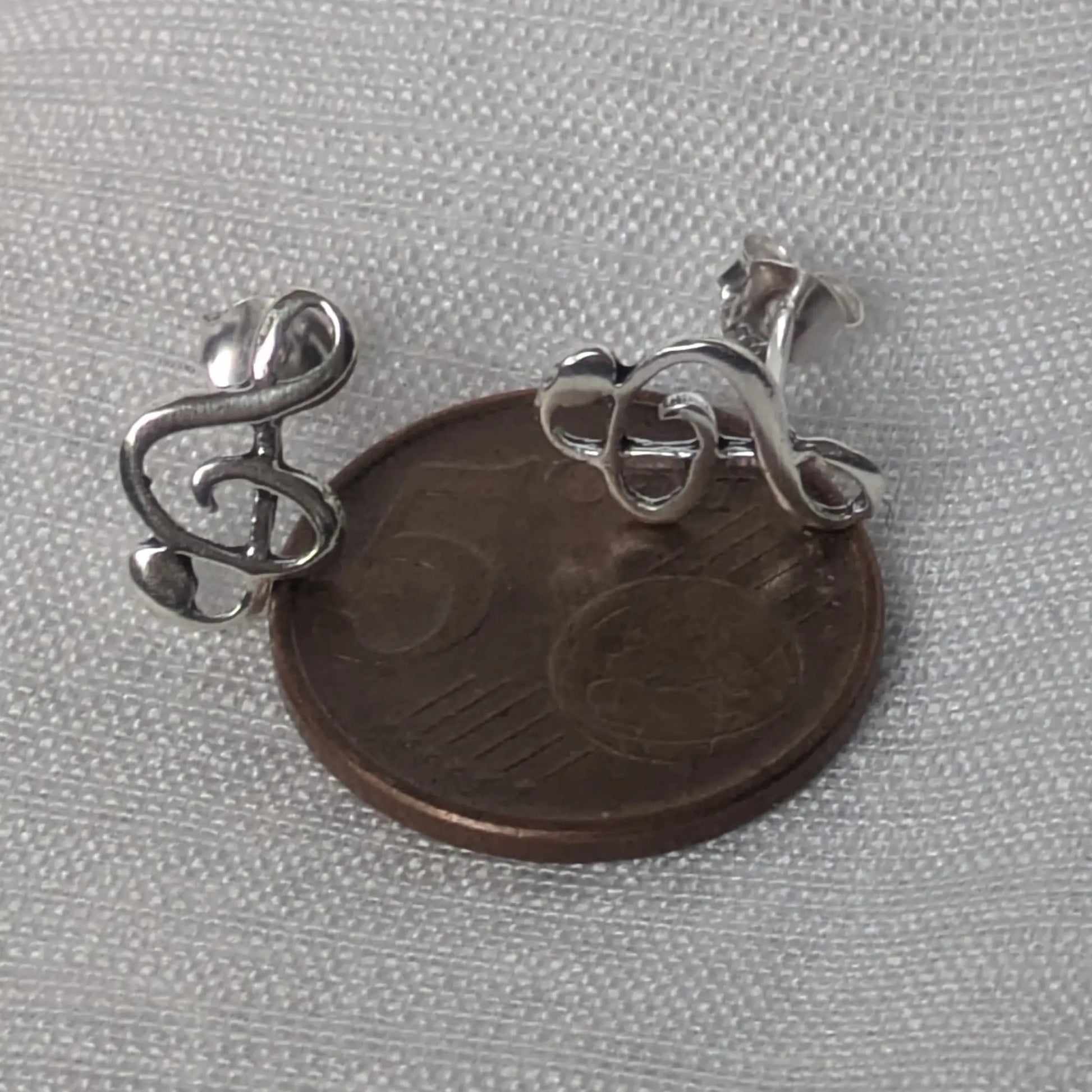 Größenvergleich der silbernen Violinschlüssel-Ohrstecker auf einer 5-Cent-Münze.