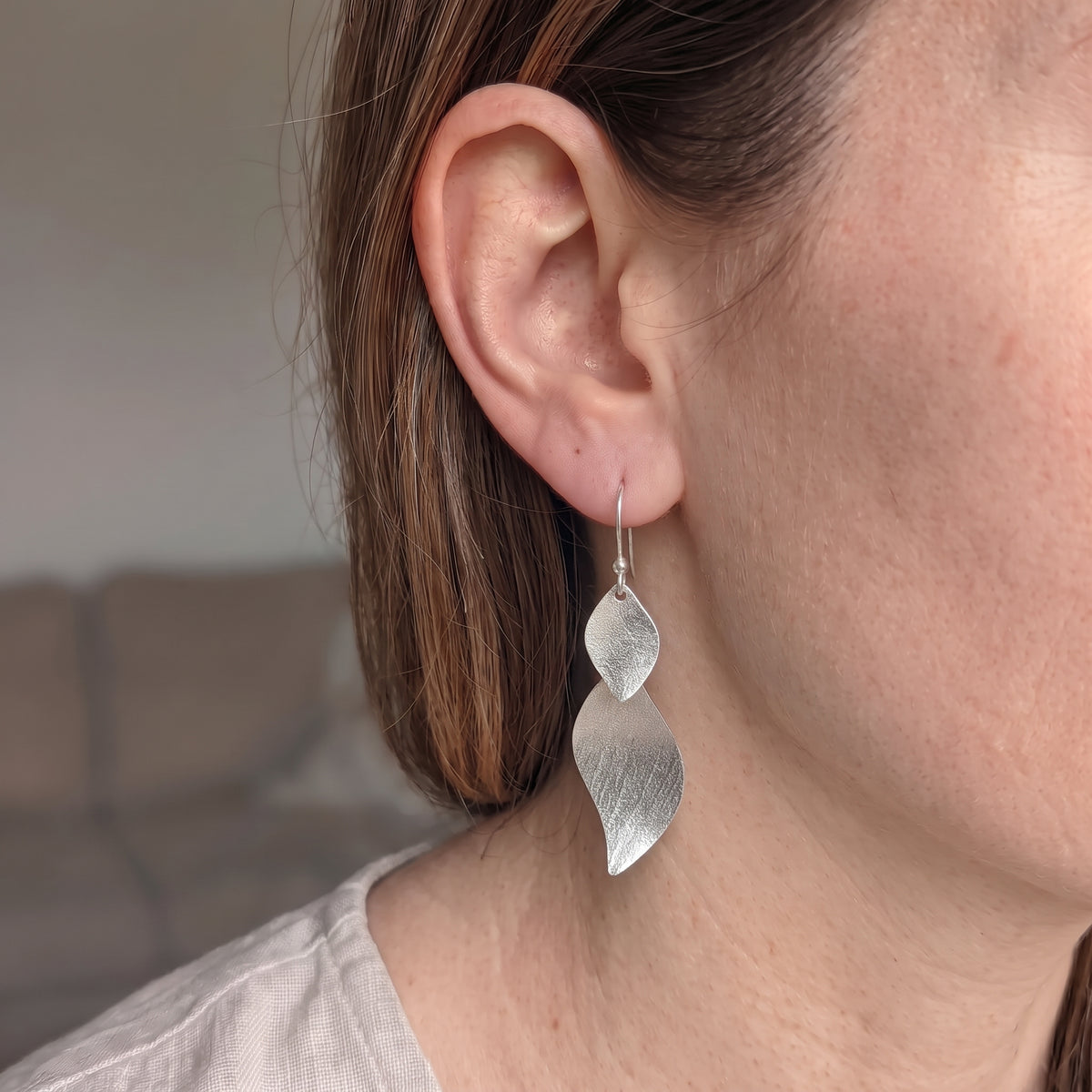 Silber-Ohrhänger mit strukturiertem Blättermotiv präsentiert ein einem Damen-Ohr.