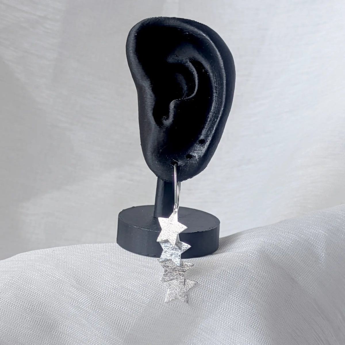 Lange Stern-Ohrhänger aus Silber getragen an einem schwarzen Ohr-Display, um den eleganten Fall der Kaskade am Ohr zu demonstrieren.

