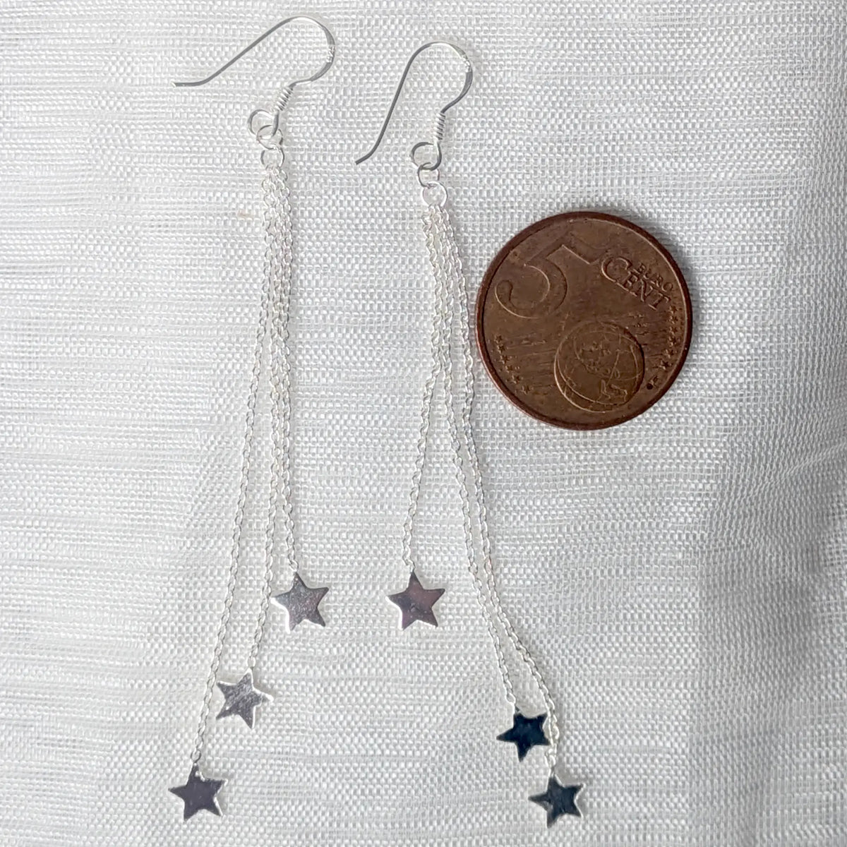 Größenvergleich: Die zarten Sterlingsilber Ketten und Stern-Anhänger der langen Ohrhänger liegen auf einer 5-Cent-Münze.