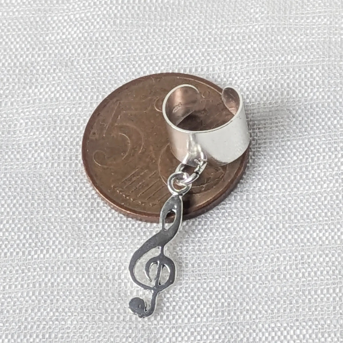 Filigrane Notenschlüssel-Ohrklemme aus echtem Silber liegend auf einer 5-Cent-Münze zum Größenvergleich.

