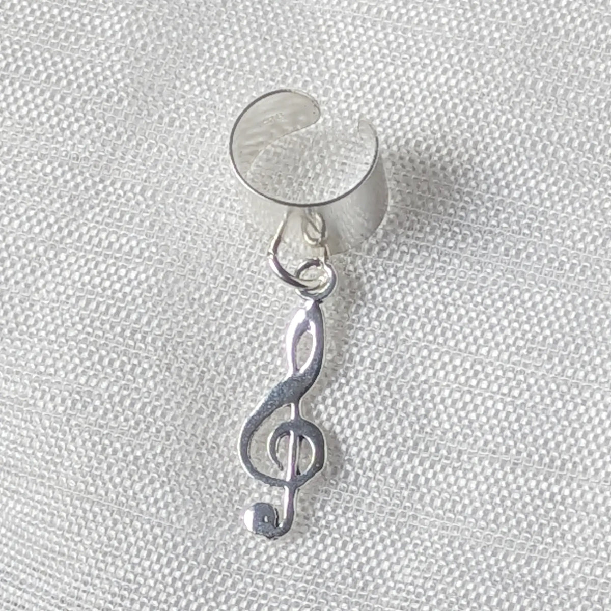 Detaillierte Nahaufnahme einer glänzenden Silber-Ohrklemme mit einem frei schwingenden Notenschlüssel-Anhänger.