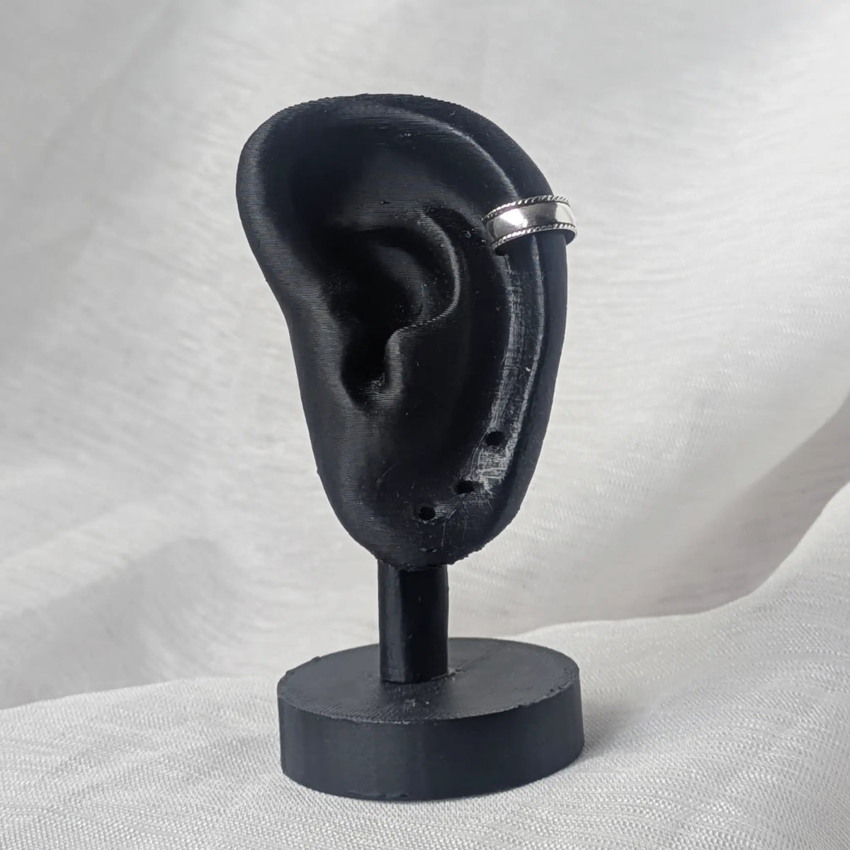 Breite Silber-Ohrklemme mit Kordelrand, getragen an der Helix-Position eines schwarzen Modell-Ohrs zur Demonstration der Passform.
