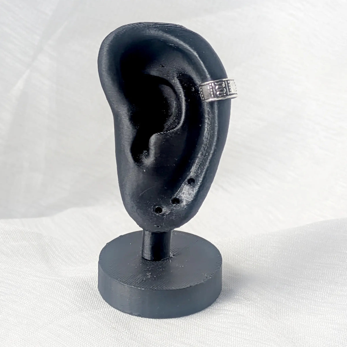 Silberner Ear Cuff getragen an der seitlichen Ohrmuschel eines schwarzen Ohr-Displays, um die Position als Fake-Piercing zu demonstrieren.
