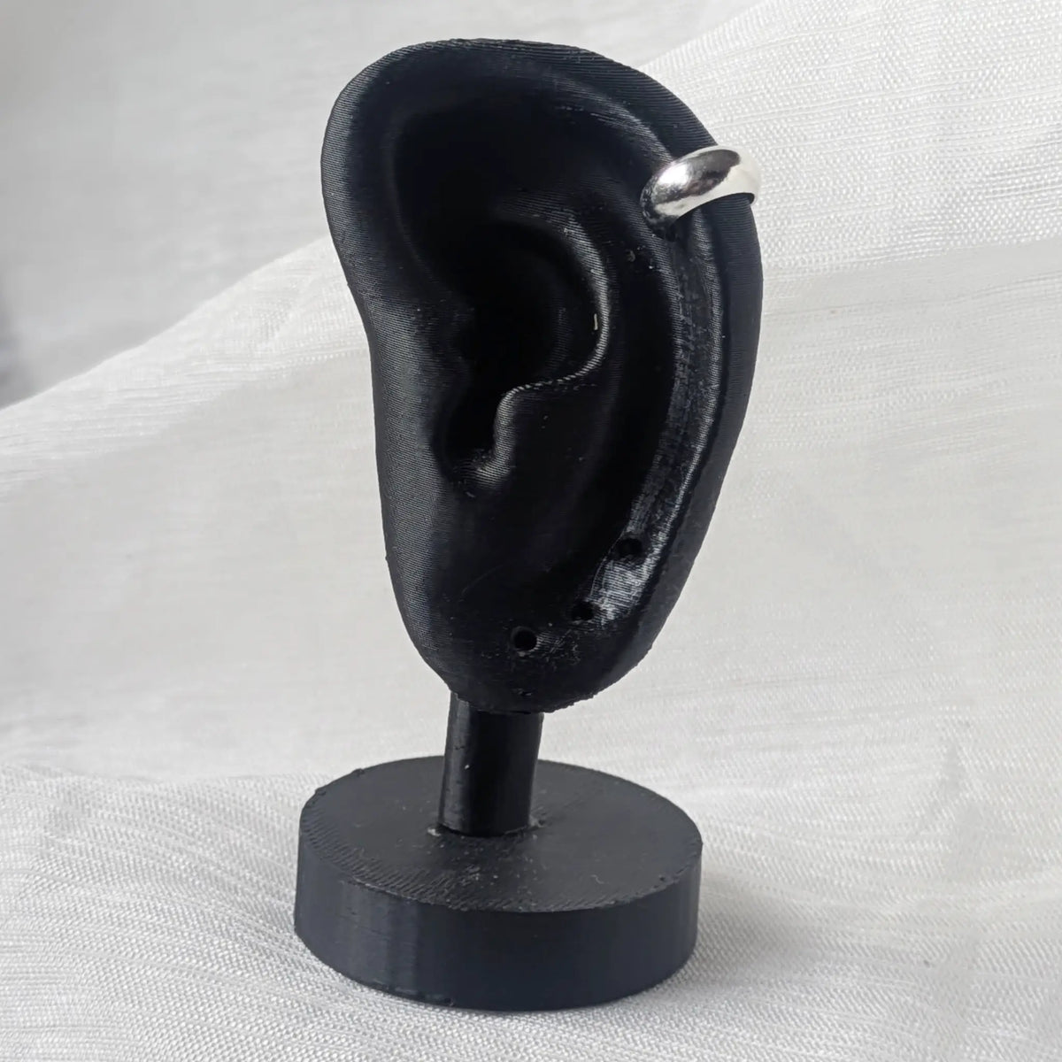 Breite, glänzende Silber-Ohrklemme, sicher befestigt am oberen Knorpel eines schwarzen Ohr-Displays.