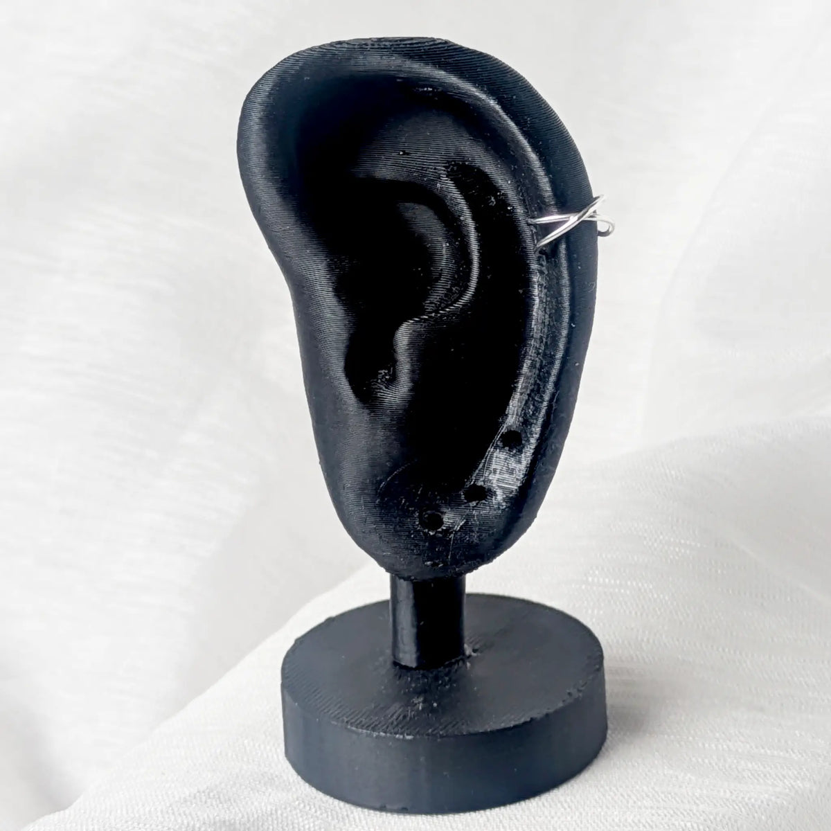 Gekreuzter Silber-Earcuff in X-Form, getragen an der Helix-Position eines schwarzen Modell-Ohrs zur Demonstration der Passform.