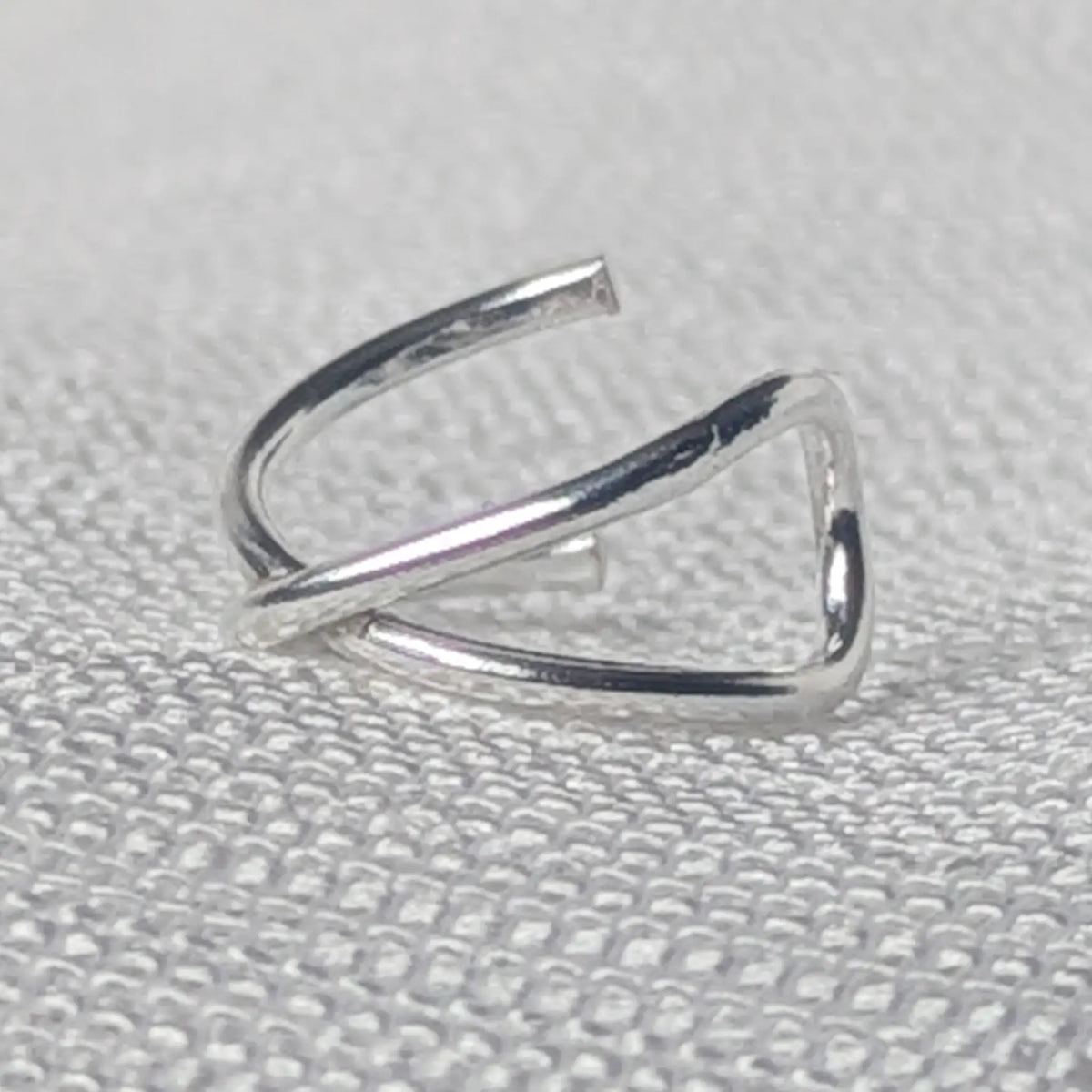 Nahaufnahme einer minimalistischen 925 Silber Ohrklemme mit hochglanzpolierter, gekreuzter X-Form.