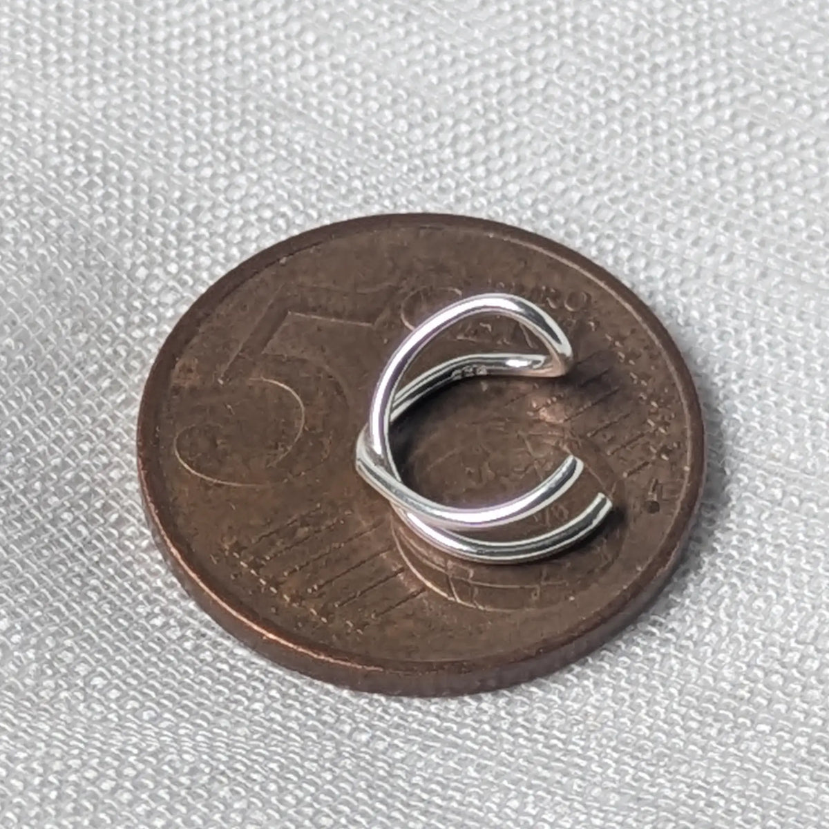 Größenvergleich: Die zierliche, gekreuzte 925 Silber Ohrklemme liegt flach auf einer 5-Cent-Münze.