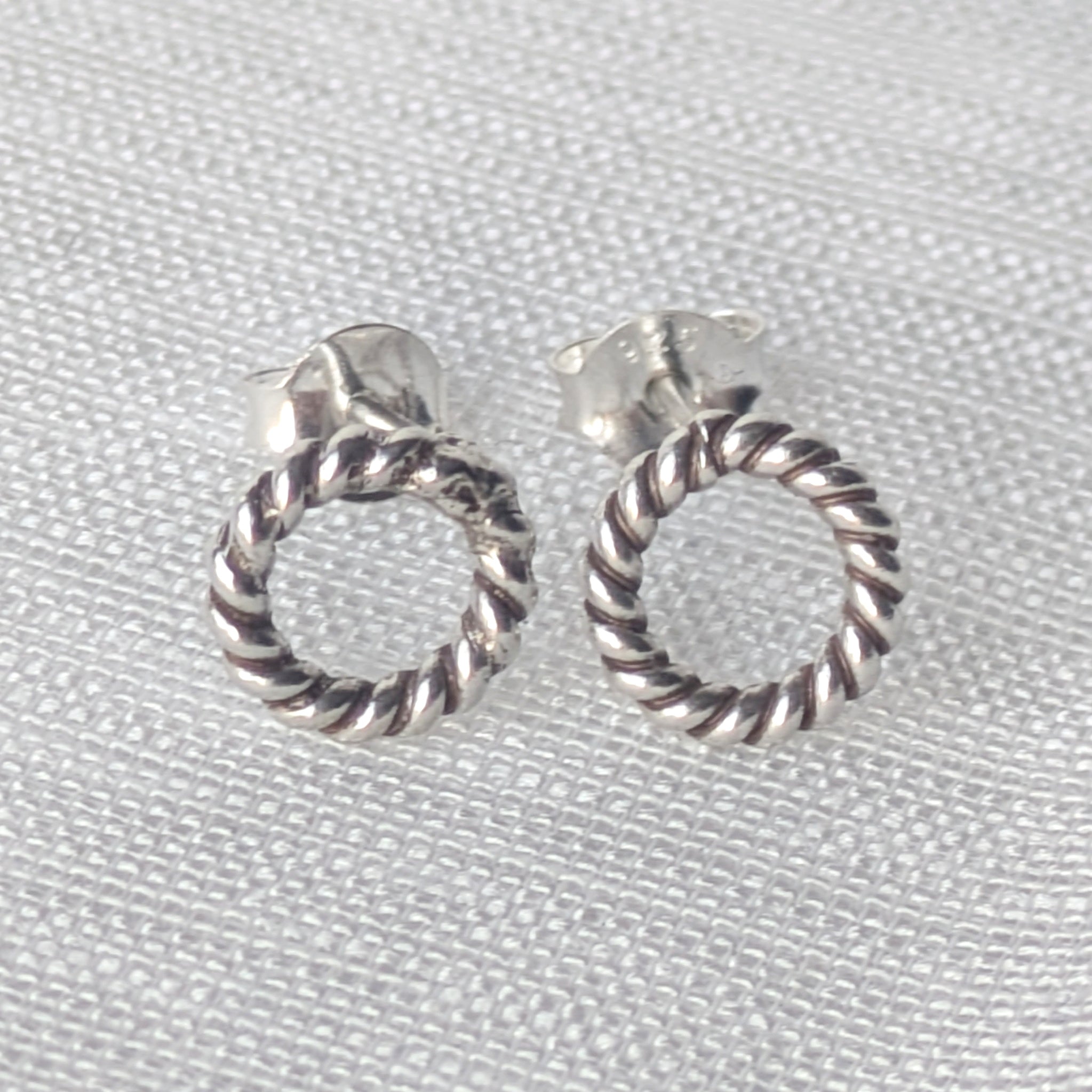 Silberne Ohrstecker mit gedrehtem Rope-Design auf weißem Stoffhintergrund