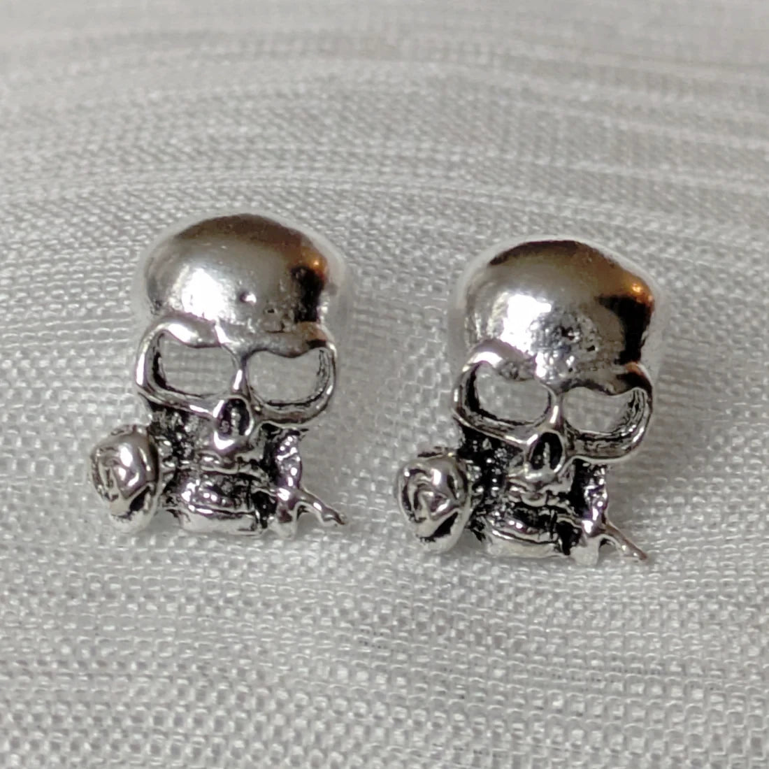 Zwei silberne Totenkopf-Ohrstecker mit Rosenmotiv im Gothic-Stil.