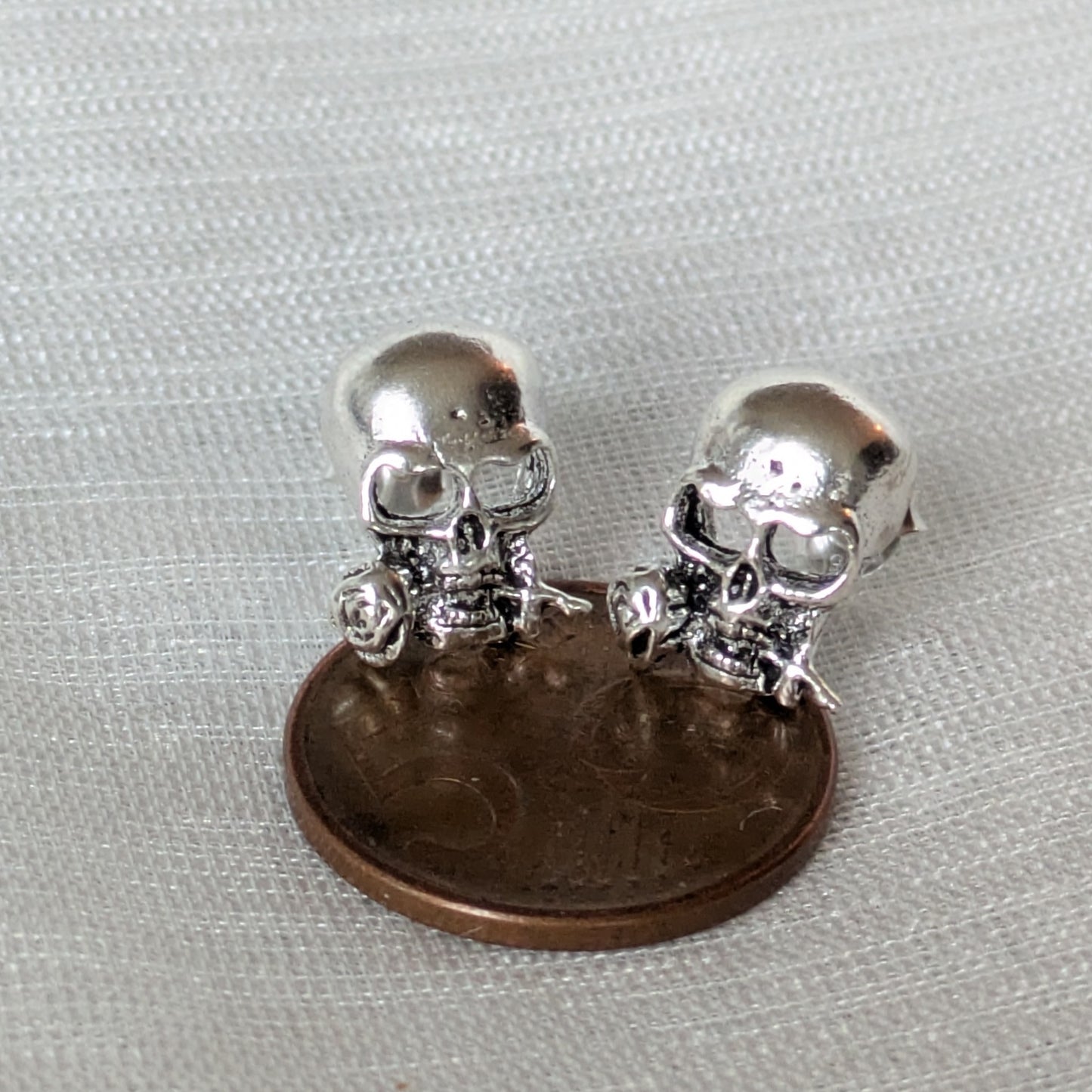 Paar silberne Ohrstecker mit Totenkopf-Motiv auf 5-Cent Münze.