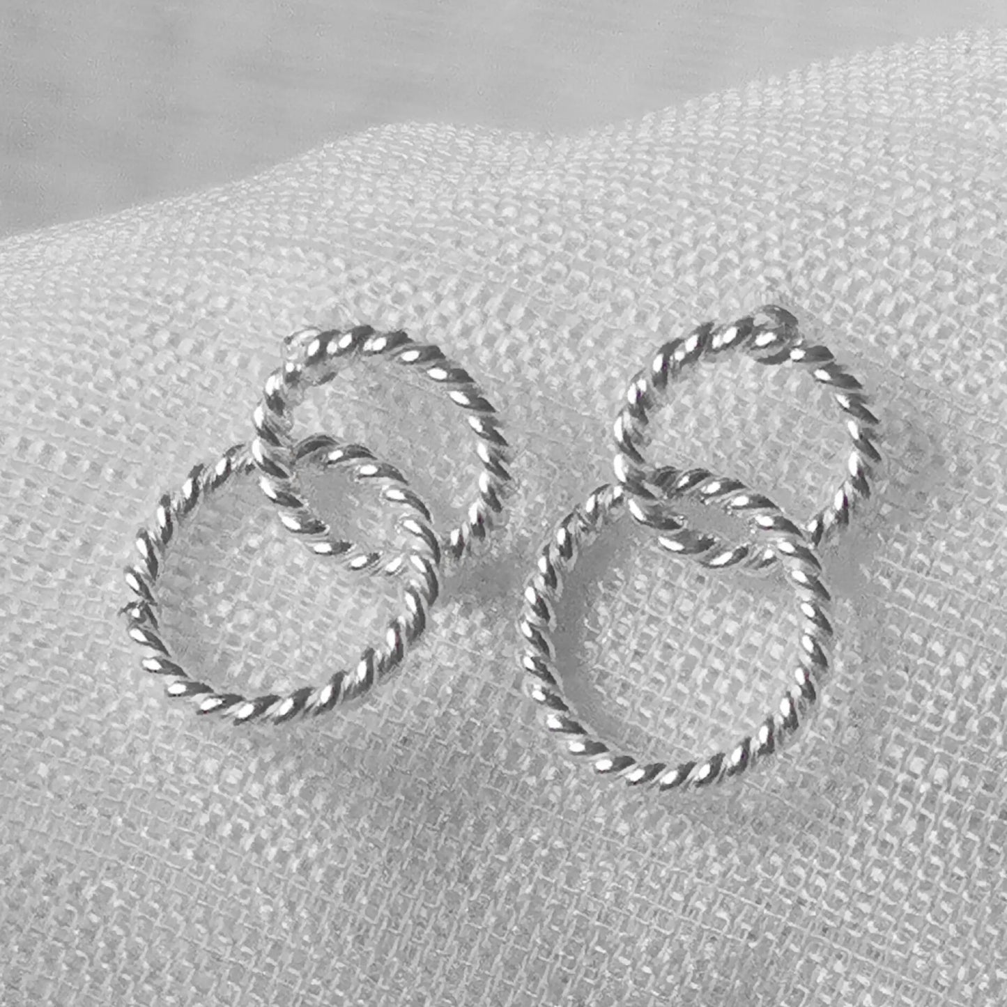 Nahaufnahme von gedrehten 925 Silber-Ohrsteckern in verschlungener Doppelkreis-Optik mit kordelter Oberflächenstruktur.