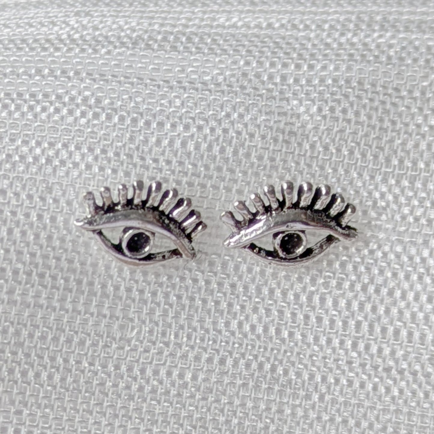 Detailaufnahme von Auge-mit-Wimpern Ohrsteckern aus poliertem Sterling-Silber.