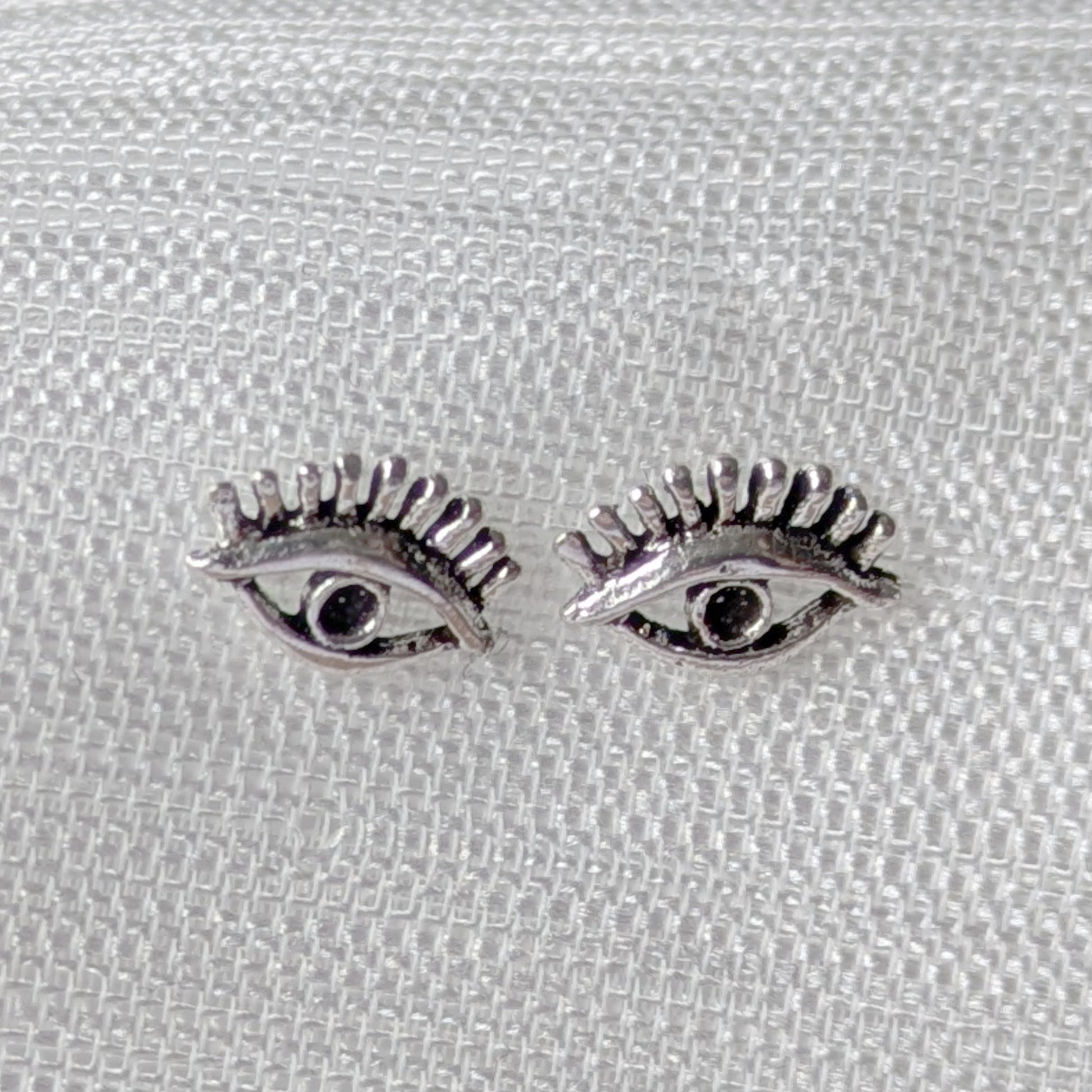 Detailaufnahme von Auge-mit-Wimpern Ohrsteckern aus poliertem Sterling-Silber.