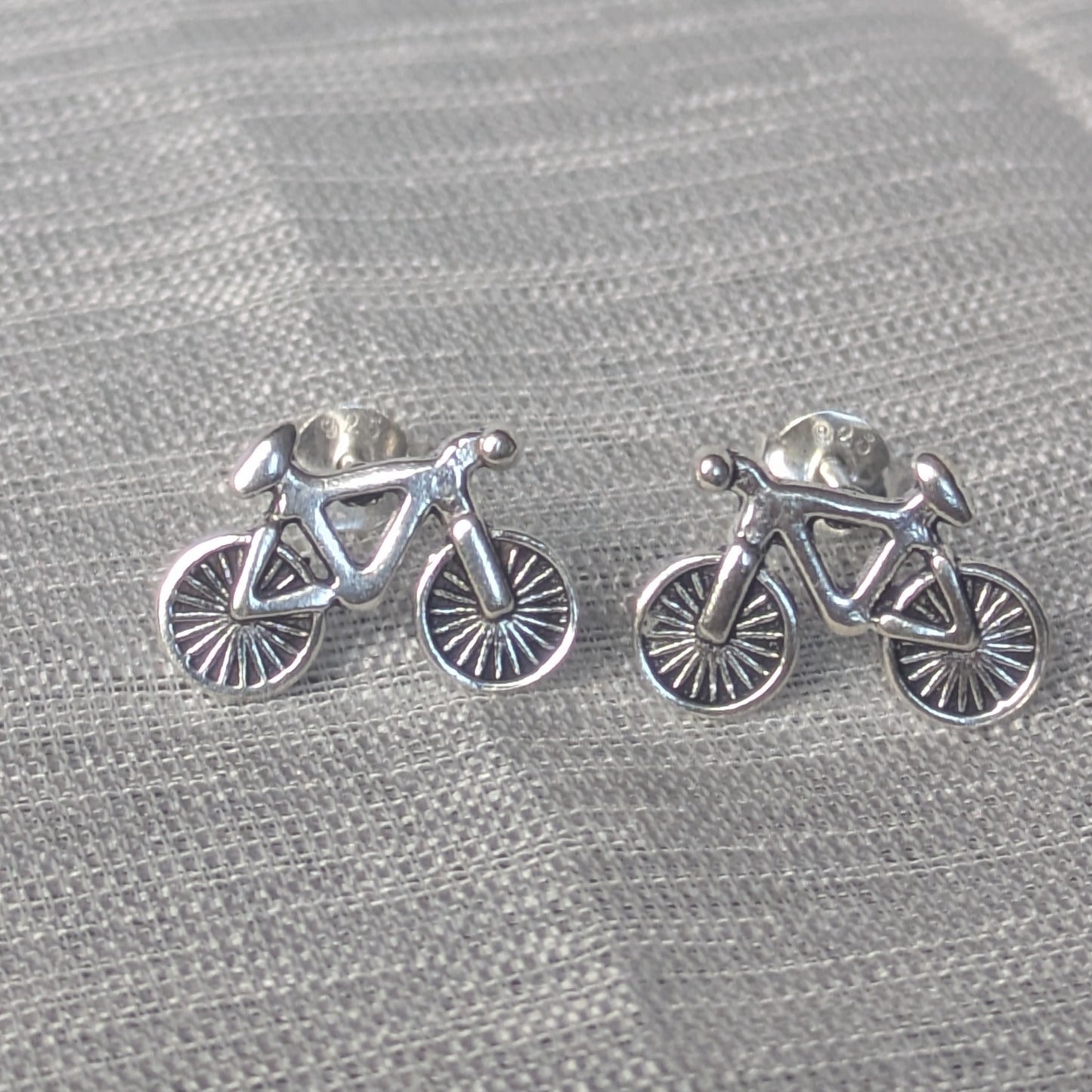 Fahrrad Ohrstecker aus 925 Silber – detailreiche Damen Ohrringe auf Stoffhintergrund