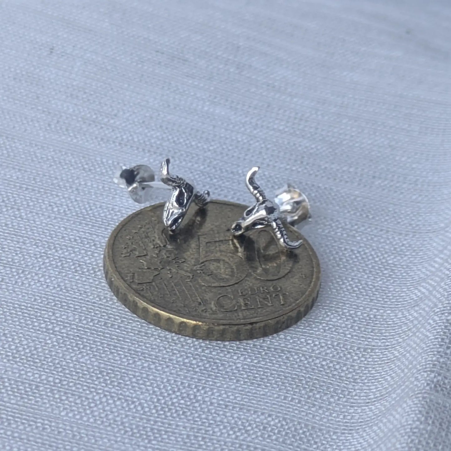 Größenvergleich der silbernen Stierschädel-Ohrstecker auf einer 5-Cent-Münze zur exakten Einschätzung der Produktgröße.