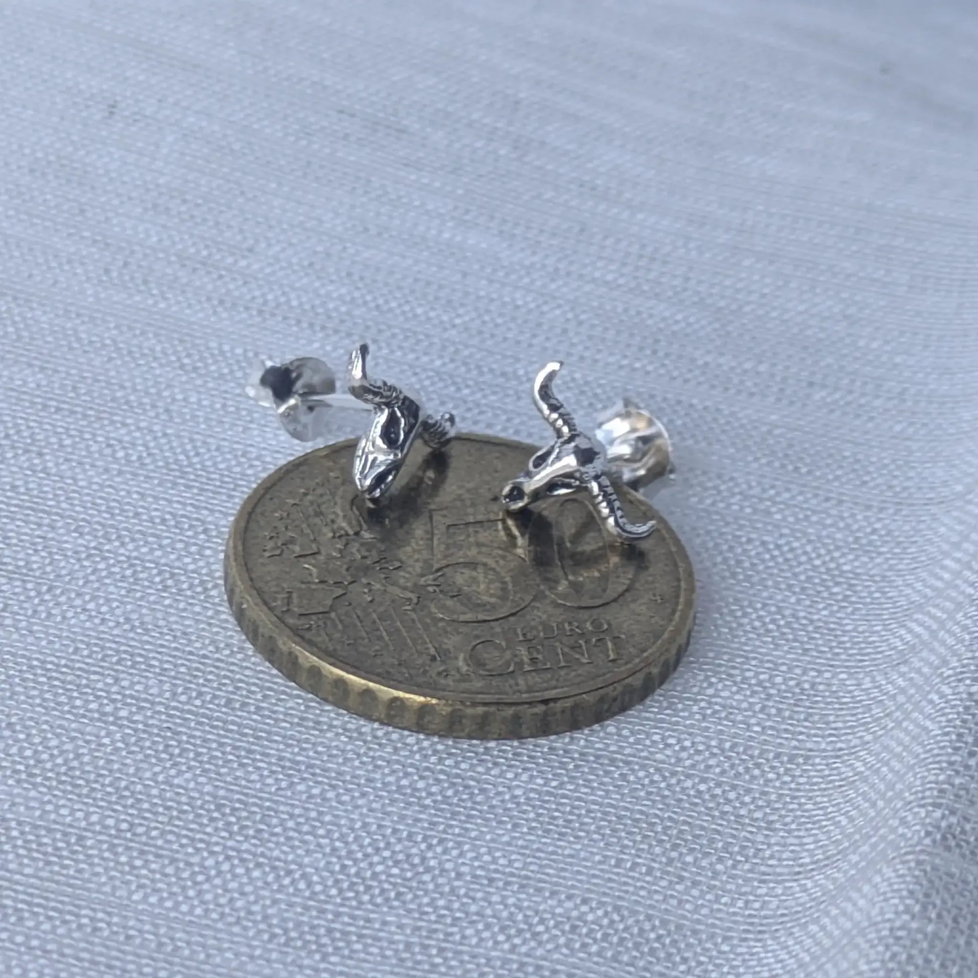 Größenvergleich der silbernen Stierschädel-Ohrstecker auf einer 5-Cent-Münze zur exakten Einschätzung der Produktgröße.