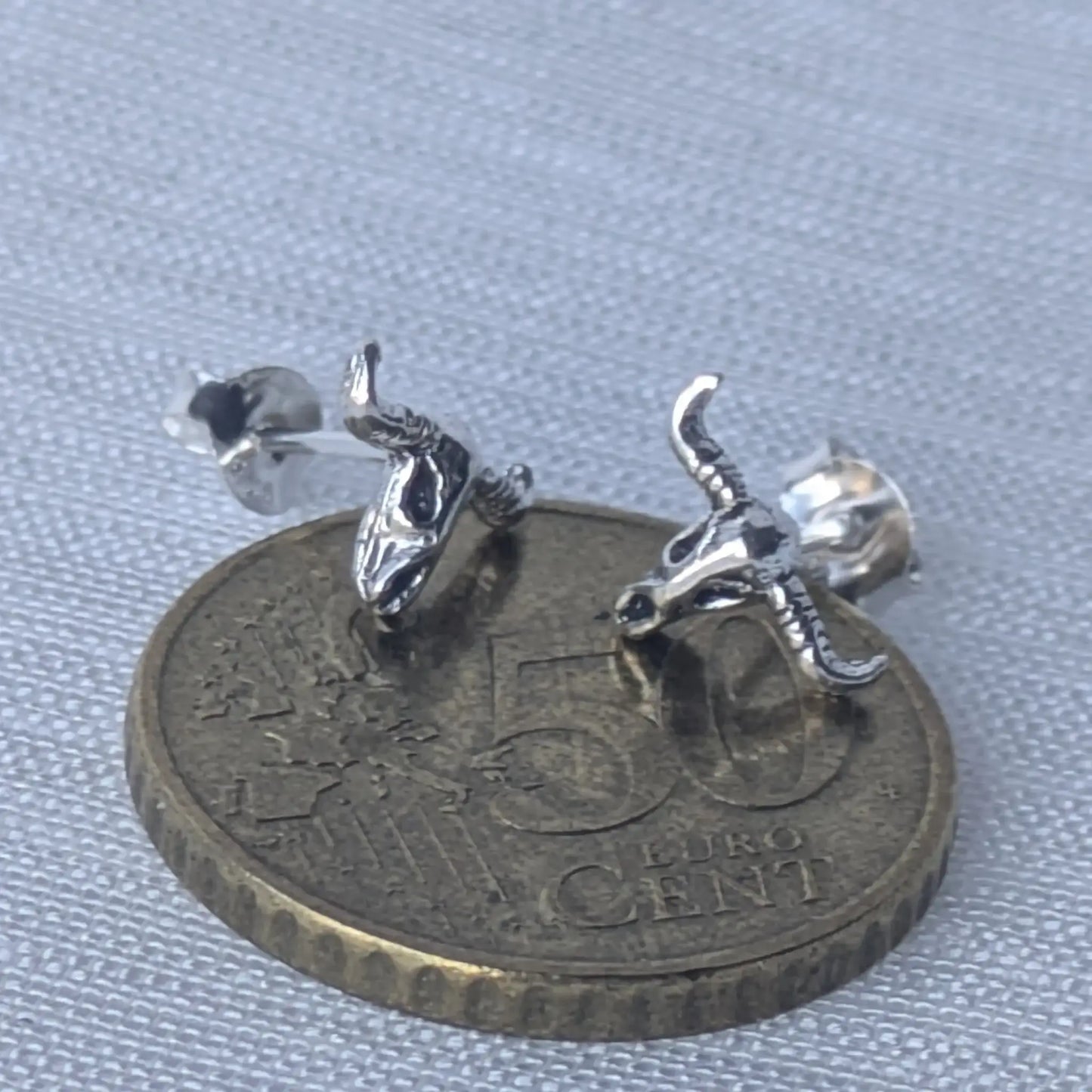 Größenvergleich der silbernen Lonrhorn-Ohrstecker auf einer 5-Cent-Münze zur besseren Einschätzung der Produktgröße.