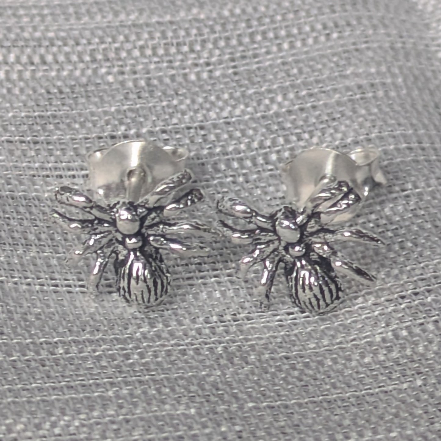 Ohrstecker aus 925 Silber in Spinnenform auf grauem Stoffhintergrund.