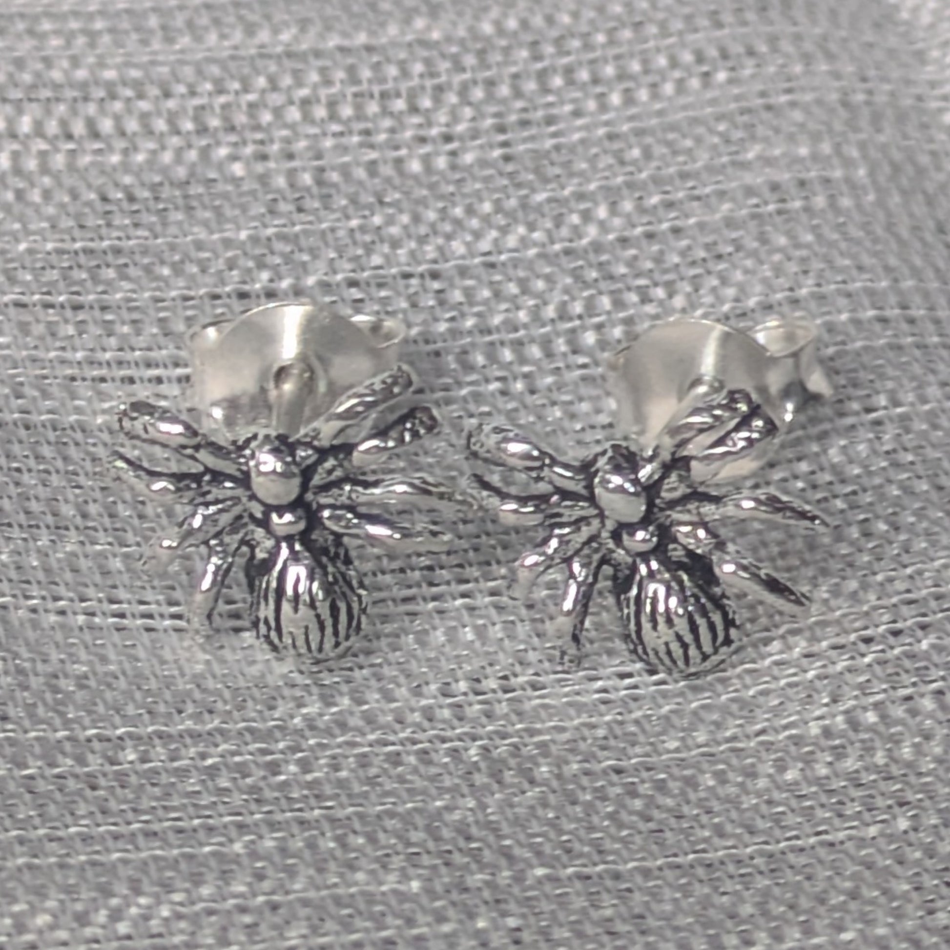 Ohrstecker aus 925 Silber in Spinnenform auf grauem Stoffhintergrund.