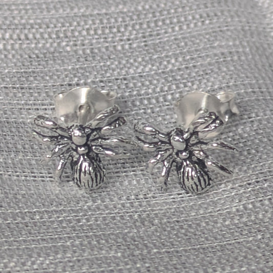 Ohrstecker aus 925 Silber in Spinnenform auf grauem Stoffhintergrund.