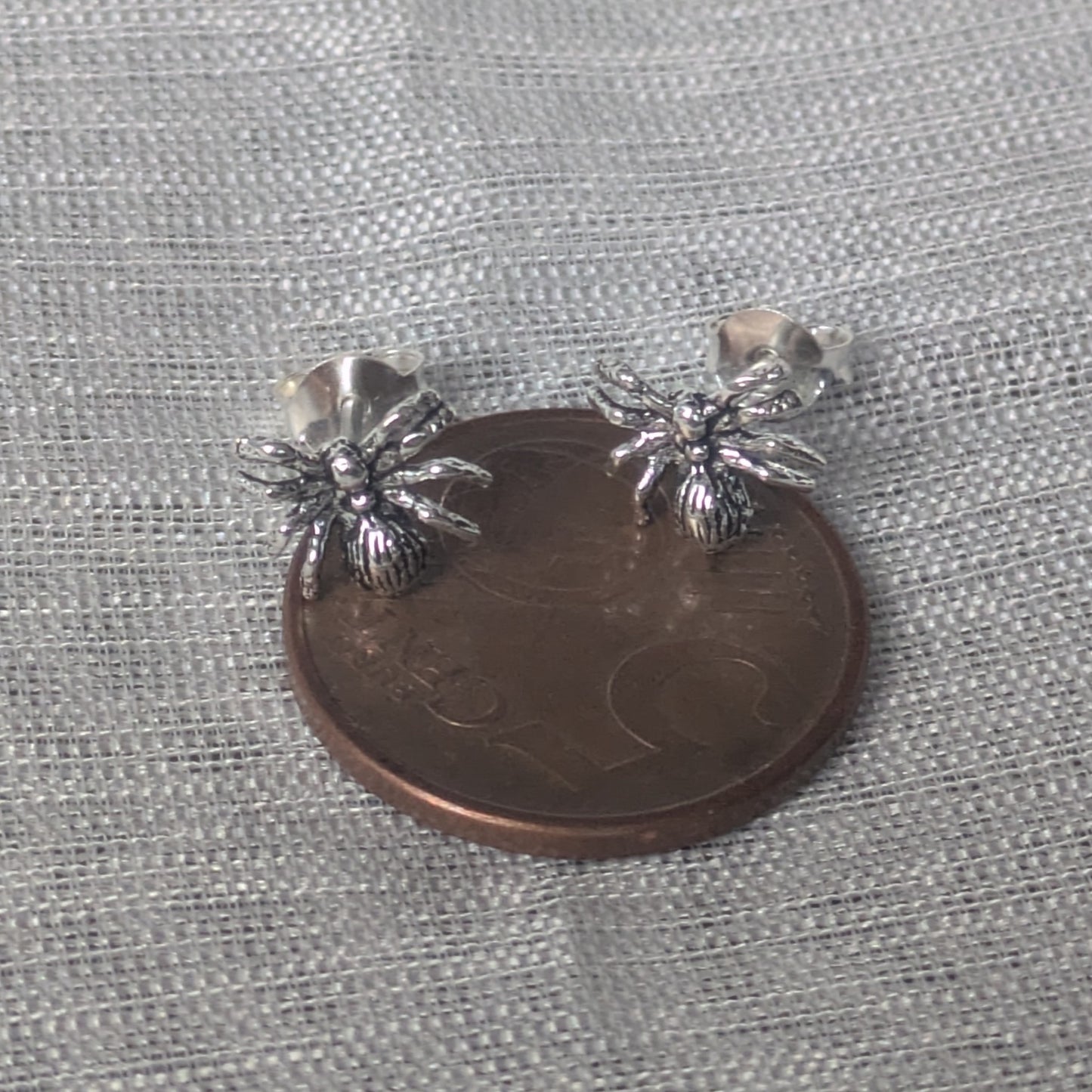 Spinnen‑Ohrstecker aus Sterling Silber, auf 5-Cent Münze frontal fotografiert.