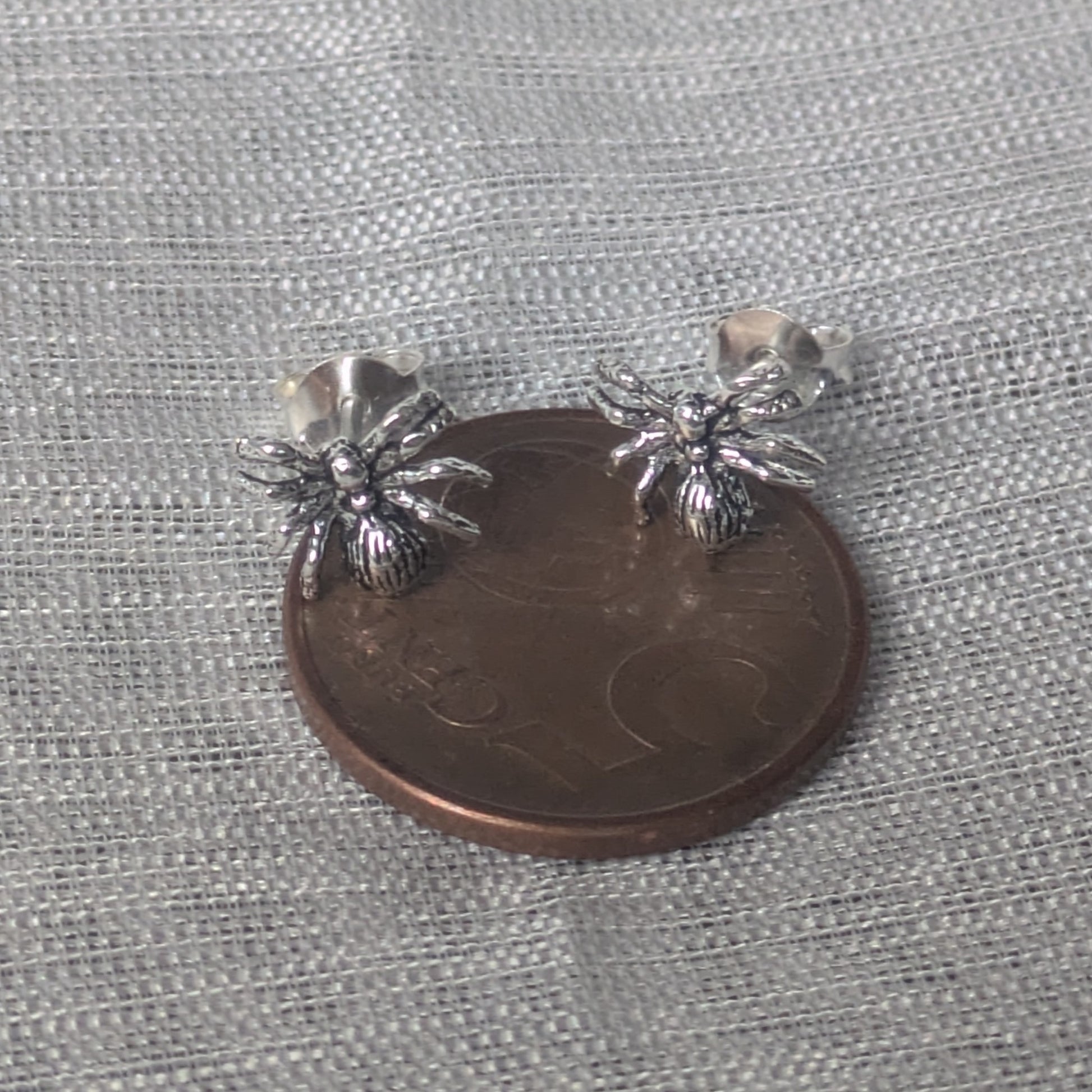 Spinnen‑Ohrstecker aus Sterling Silber, auf 5-Cent Münze frontal fotografiert.